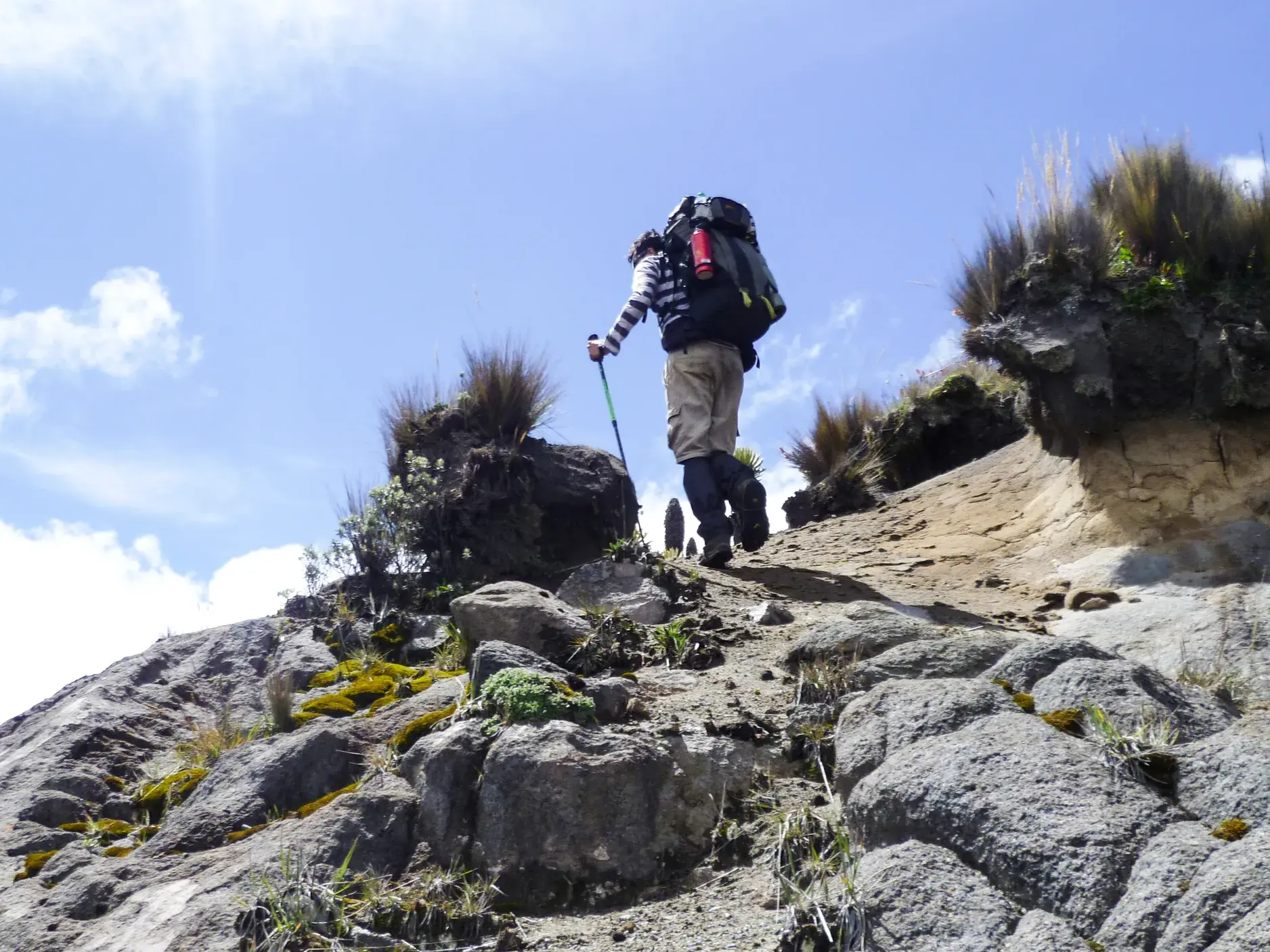 Ein Trekker mit großem Rucksack steigt einen steilen, felsigen Hang im Los Nevados-Nationalpark in Kolumbien hinauf.