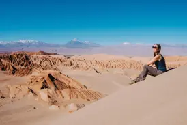 Eine junge Reisende genießt den Ausblick von einer Düne im Mondtal auf die Atacamawüste und Anden mit Vulkan Licancabur.