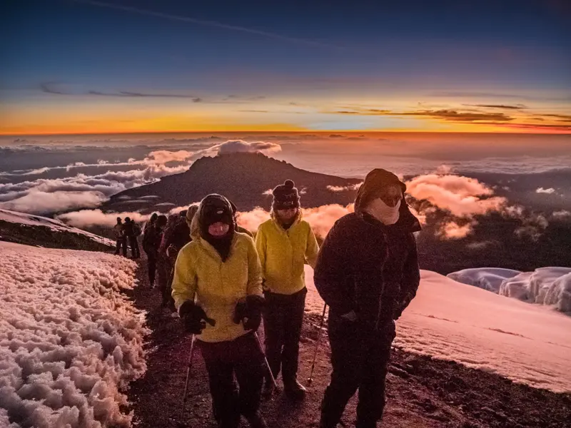 Trekking-Gruppe wandert bei Sonnenaufgang auf einem schneebedeckten Pfad am Kraterrand des Kilimanjaro zum Uhuru Peak.