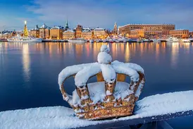 Eine schneebedeckte goldene Krone auf der Skeppsholmsbron-Brücke mit Blick auf die beleuchtete Altstadt Gamla Stan in Stockholm.