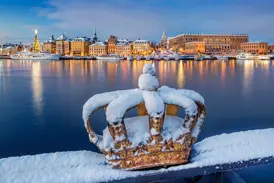 Eine schneebedeckte goldene Krone auf der Skeppsholmsbron-Brücke mit Blick auf die beleuchtete Altstadt Gamla Stan in Stockholm.