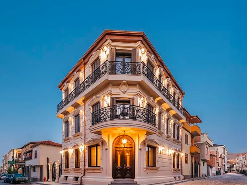 Beleuchtetes neoklassizistisches Gebäude des Artic Boutique Hotels in Korca mit schmiedeeisernen Balkonen vor blauem Abendhimmel.