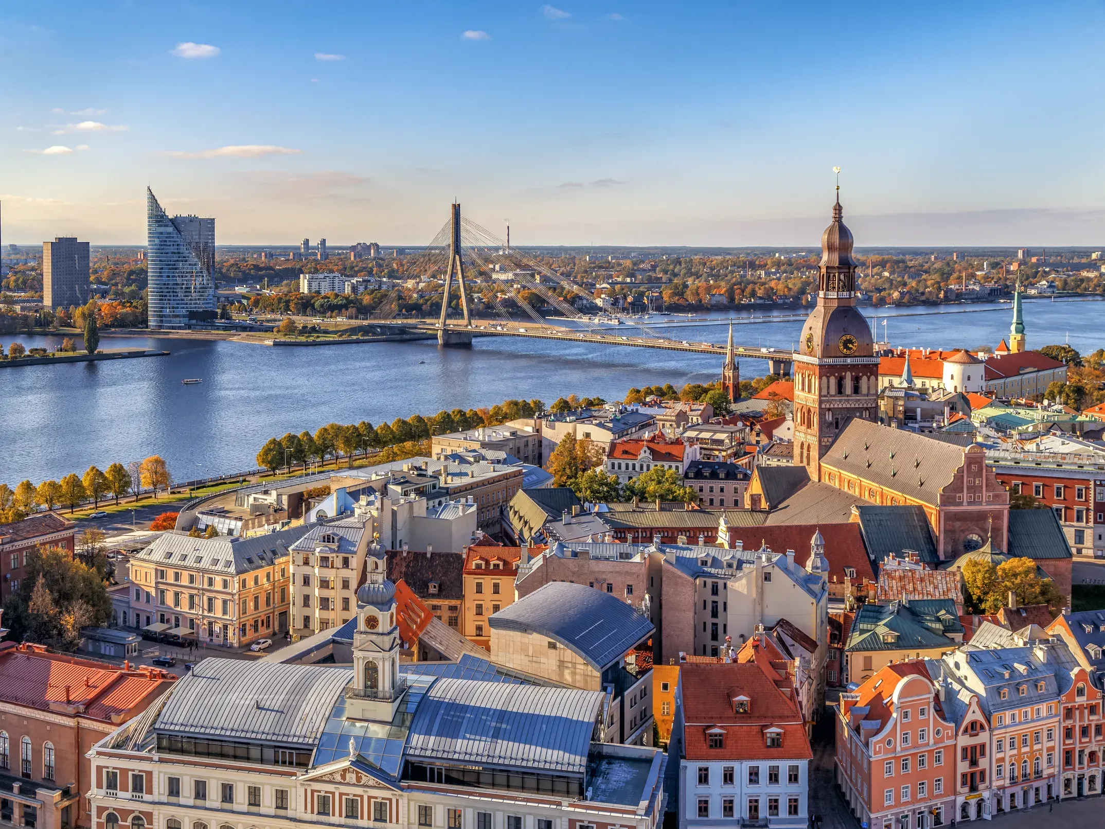 Blick über die Dächer der historischen Altstadt von Riga mit dem Dom, dem Fluss Daugava und der modernen Skyline im Hintergrund.