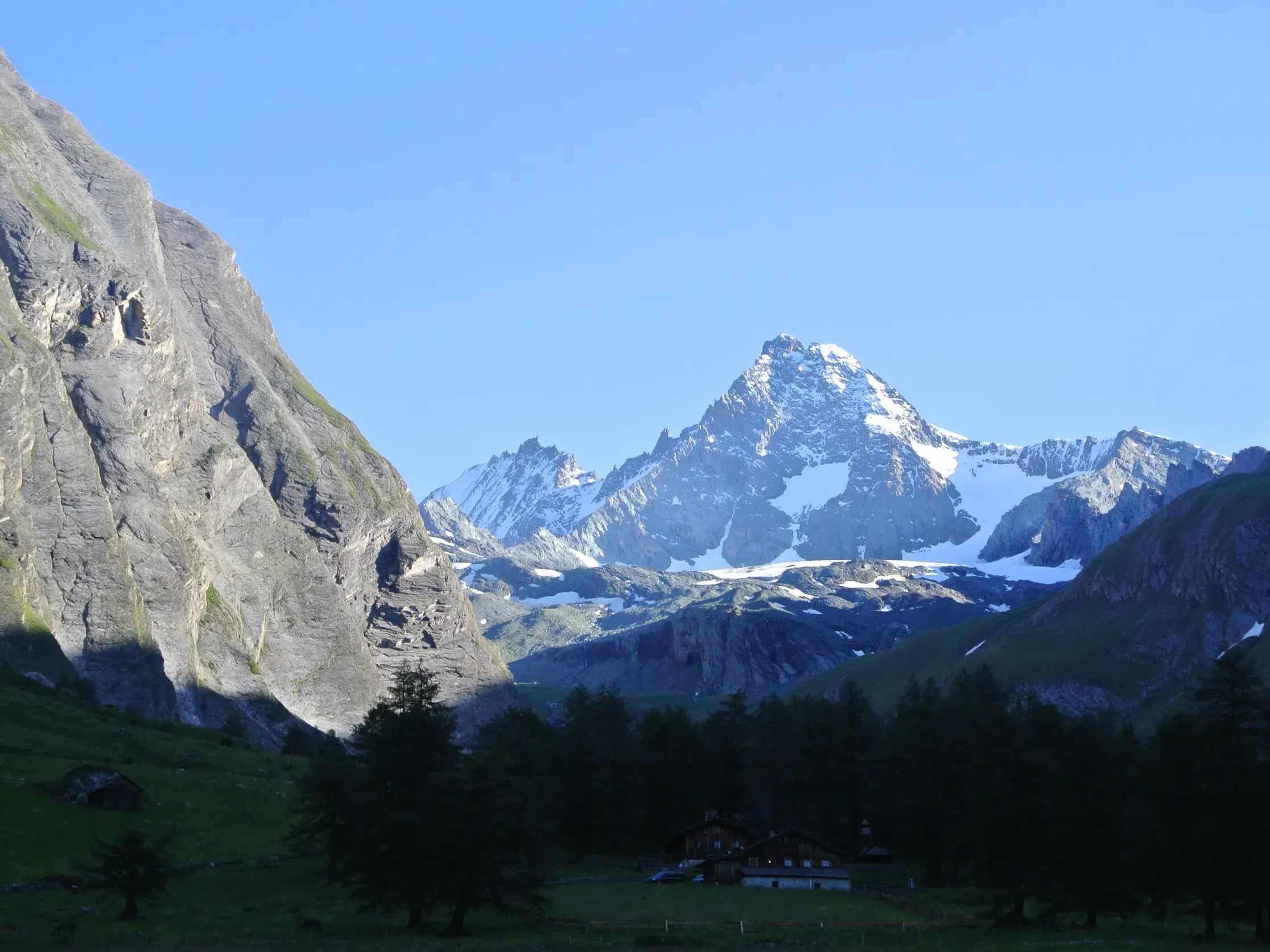 Der schneebedeckte Gipfel des Großglockner ragt über einem grünen Tal mit einer Berghütte im Nationalpark Hohe Tauern auf.
