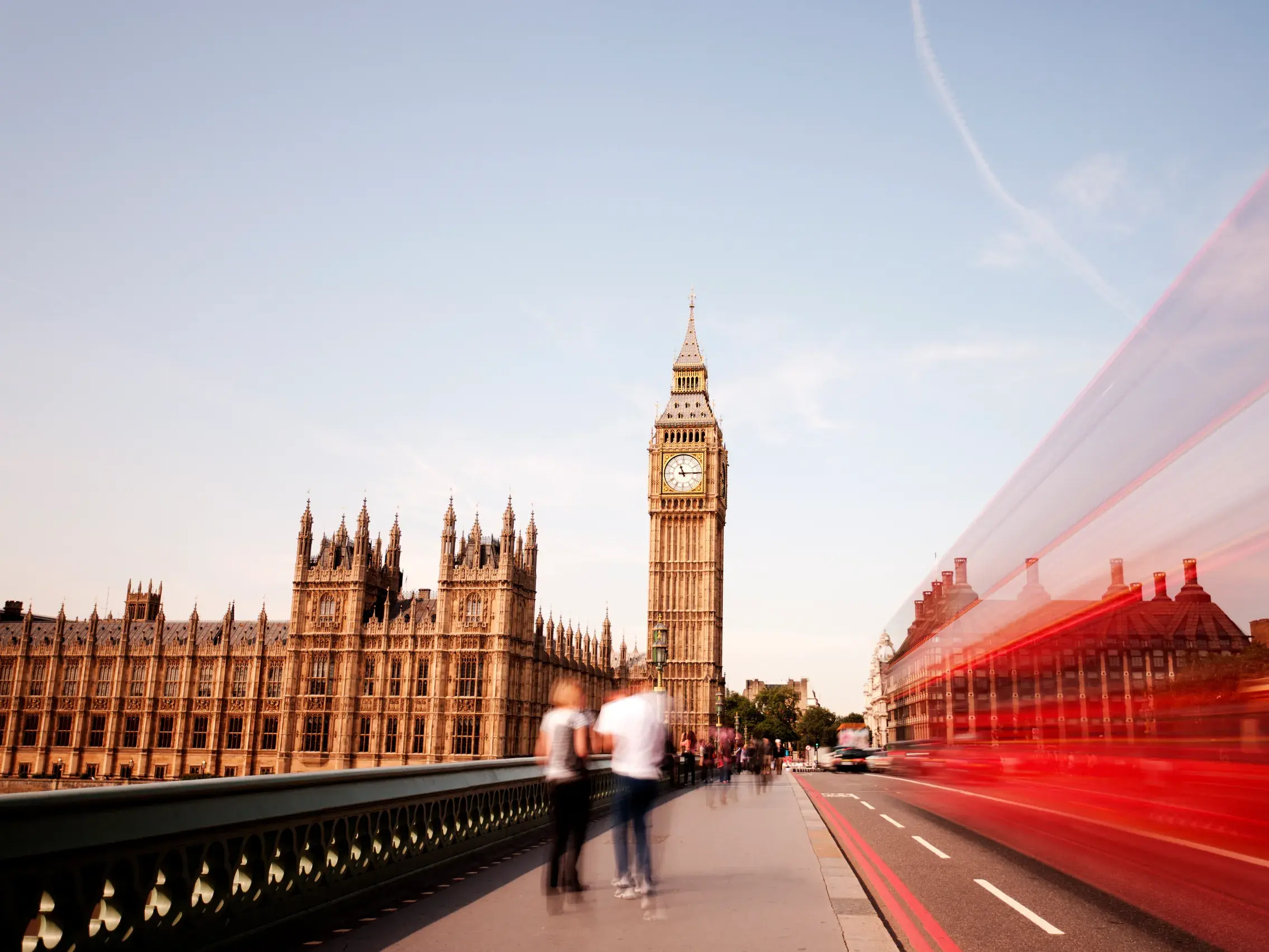 Der Uhrturm Big Ben in Westminster, London, bei Tag. Ein roter Doppeldecker-Bus erzeugt eine dynamische Bewegungsunschärfe.