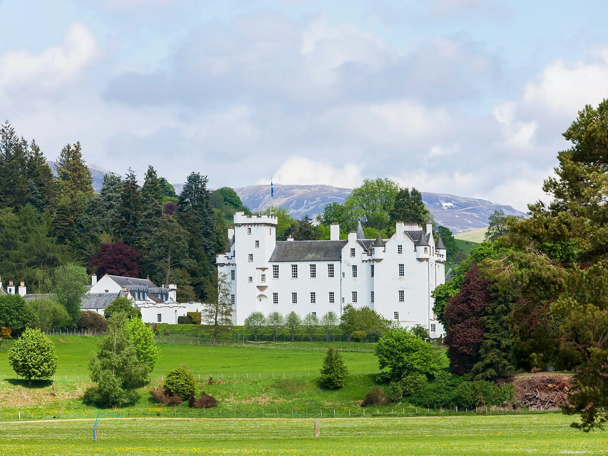 Das strahlend weiße Blair Castle vor der Bergkulisse der schottischen Highlands, umgeben von grünen Wiesen und Wäldern.