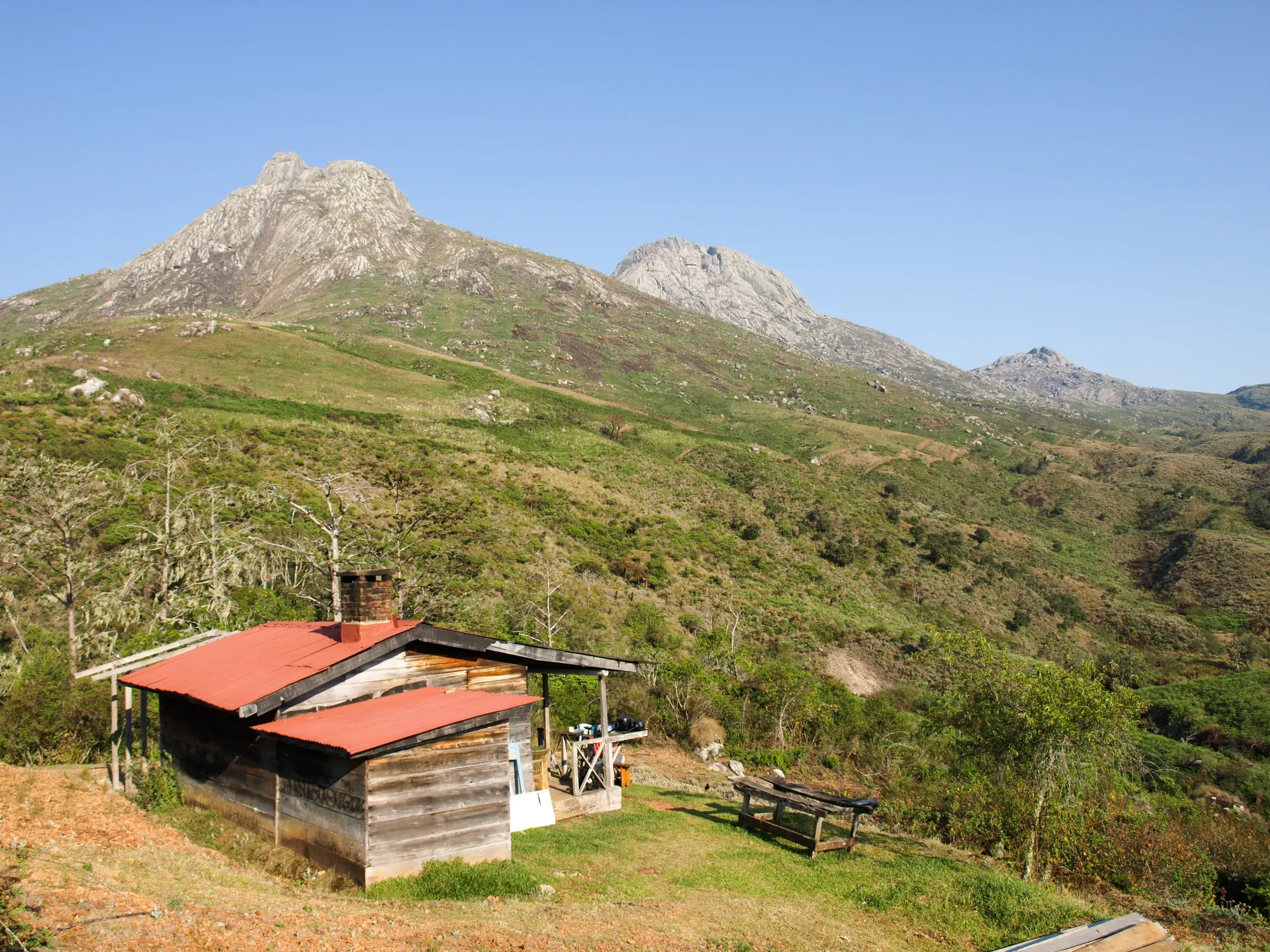 Rustikale Berghütte mit rotem Dach in den grünen Weiten des Mulanje-Massivs in Malawi bei einer Hauser Trekking-Reise.