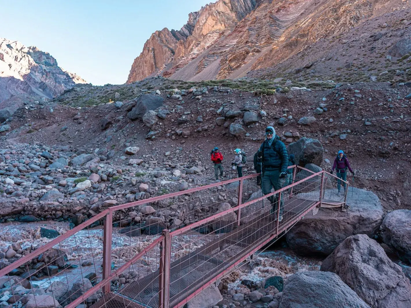 Eine Trekking-Gruppe überquert auf einer Brücke den Horcones-Fluss in der kargen Berglandschaft des Aconcagua-Provinzparks.