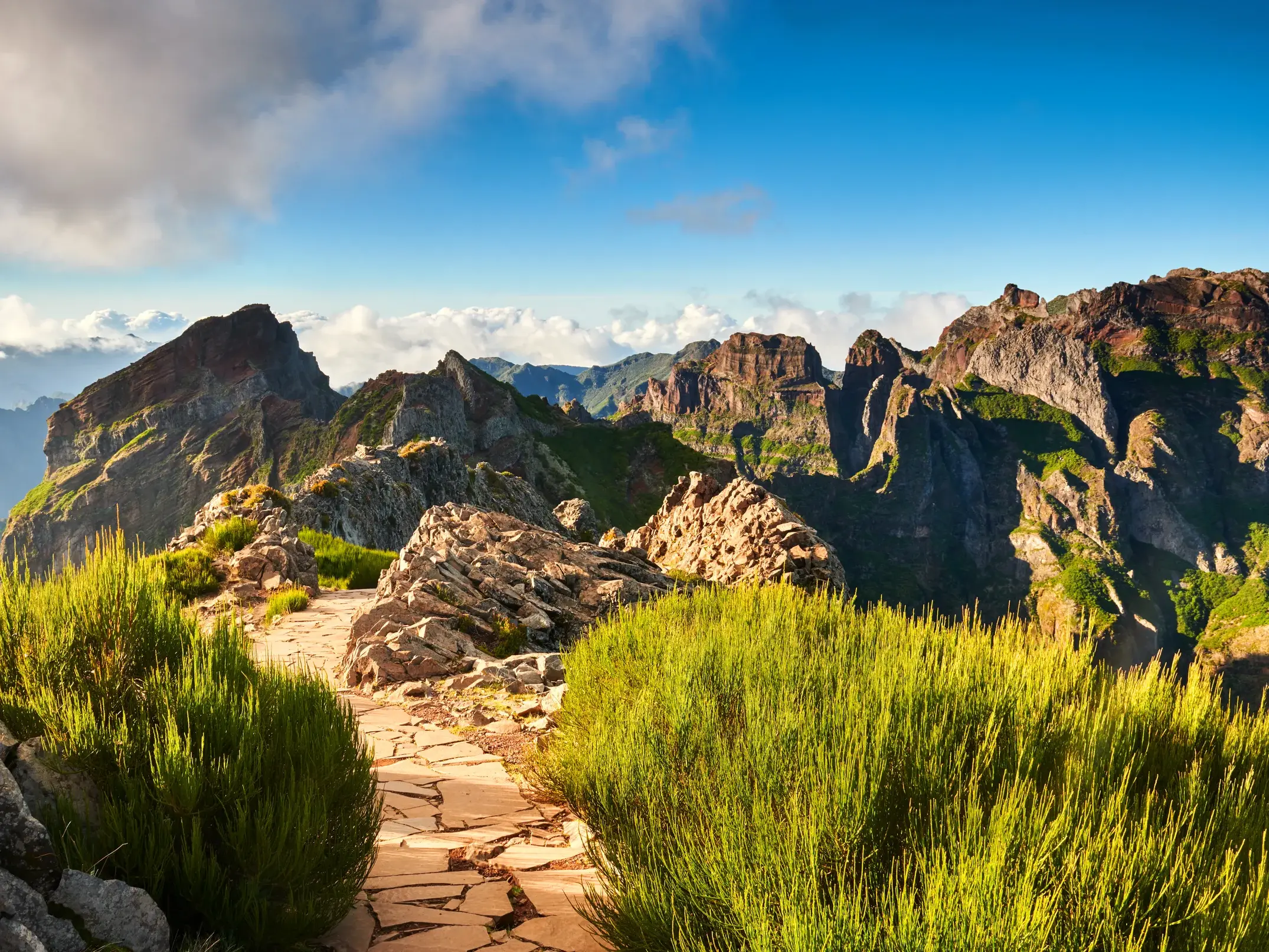 Spektakulärer Ausblick vom Wanderweg am Pico do Arieiro auf die grün bewachsenen Vulkangipfel von Madeira bei Sonnenschein.