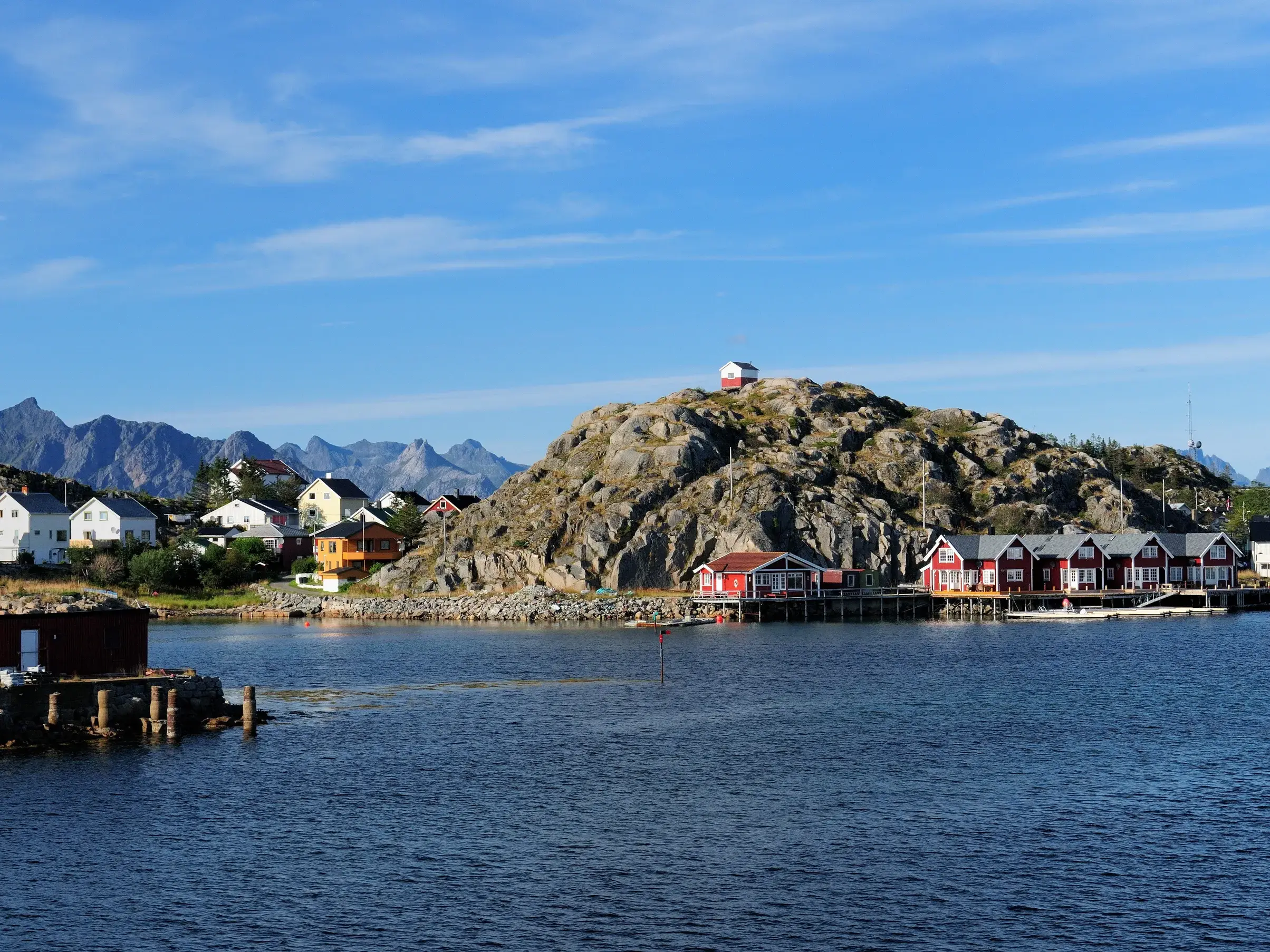 Malerisches Fischerdorf Henningsvær mit roten Rorbu-Häusern am Fjord und schroffen Bergen der Lofoten im Hintergrund.