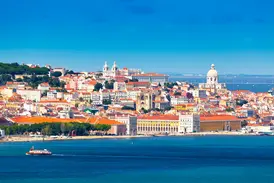 Malerischer Blick über den Rio Tejo auf die sonnige Altstadt Alfama in Lissabon mit einer Fähre im Vordergrund.