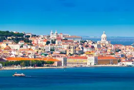 Malerischer Blick über den Rio Tejo auf die sonnige Altstadt Alfama in Lissabon mit einer Fähre im Vordergrund.