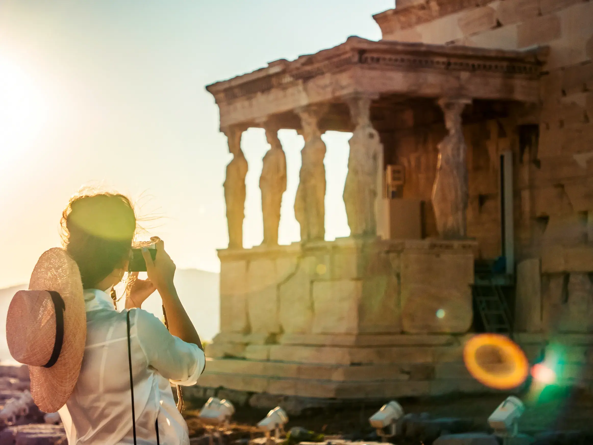 Frau mit Strohhut fotografiert die berühmten Karyatiden des Erechtheions auf der Akropolis in Athen bei Abendsonne.