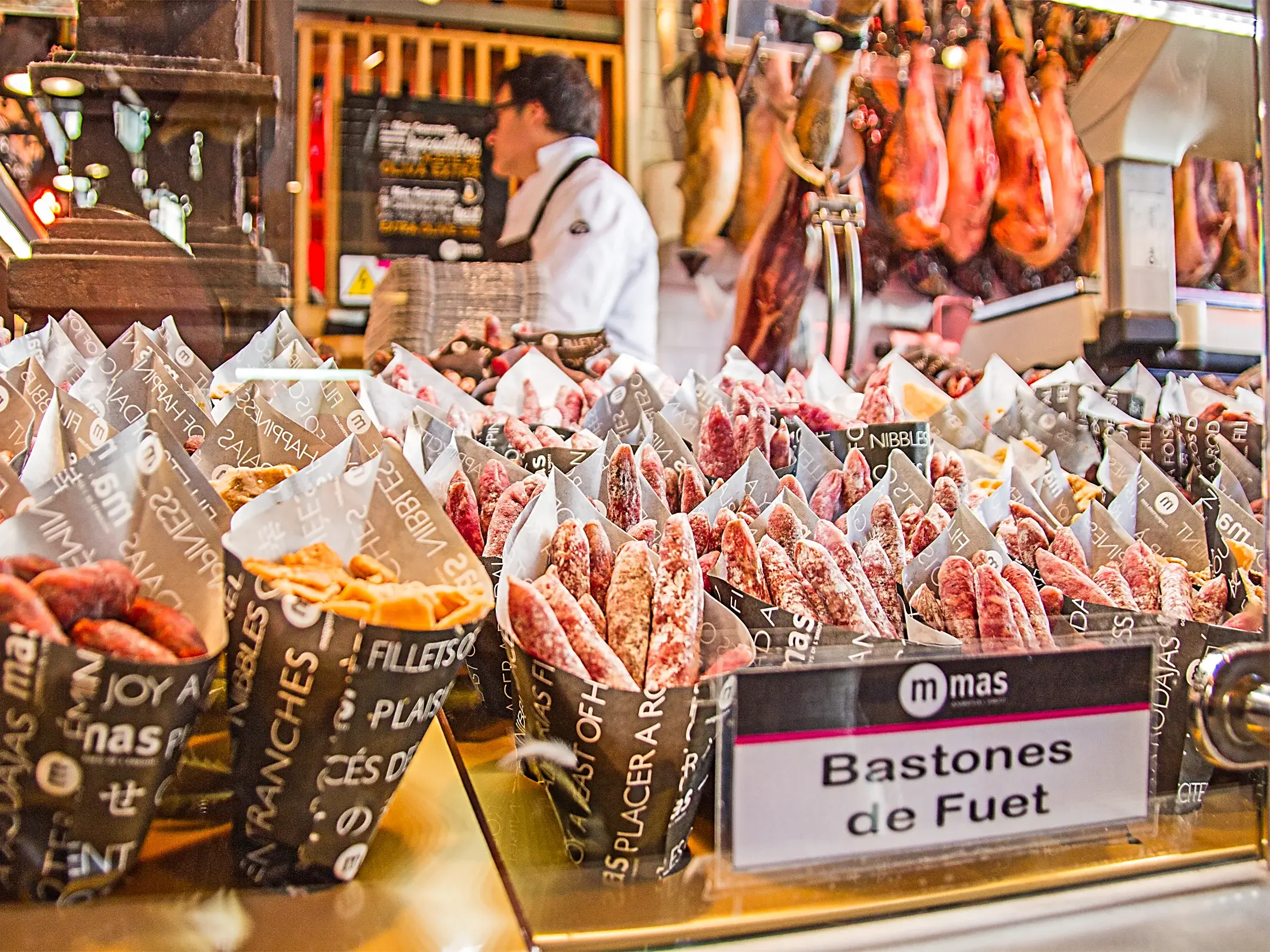 Auslage mit Bastones de Fuet und anderen spanischen Würsten im Schinkenmuseum in Madrid, im Hintergrund hängen Schinken.