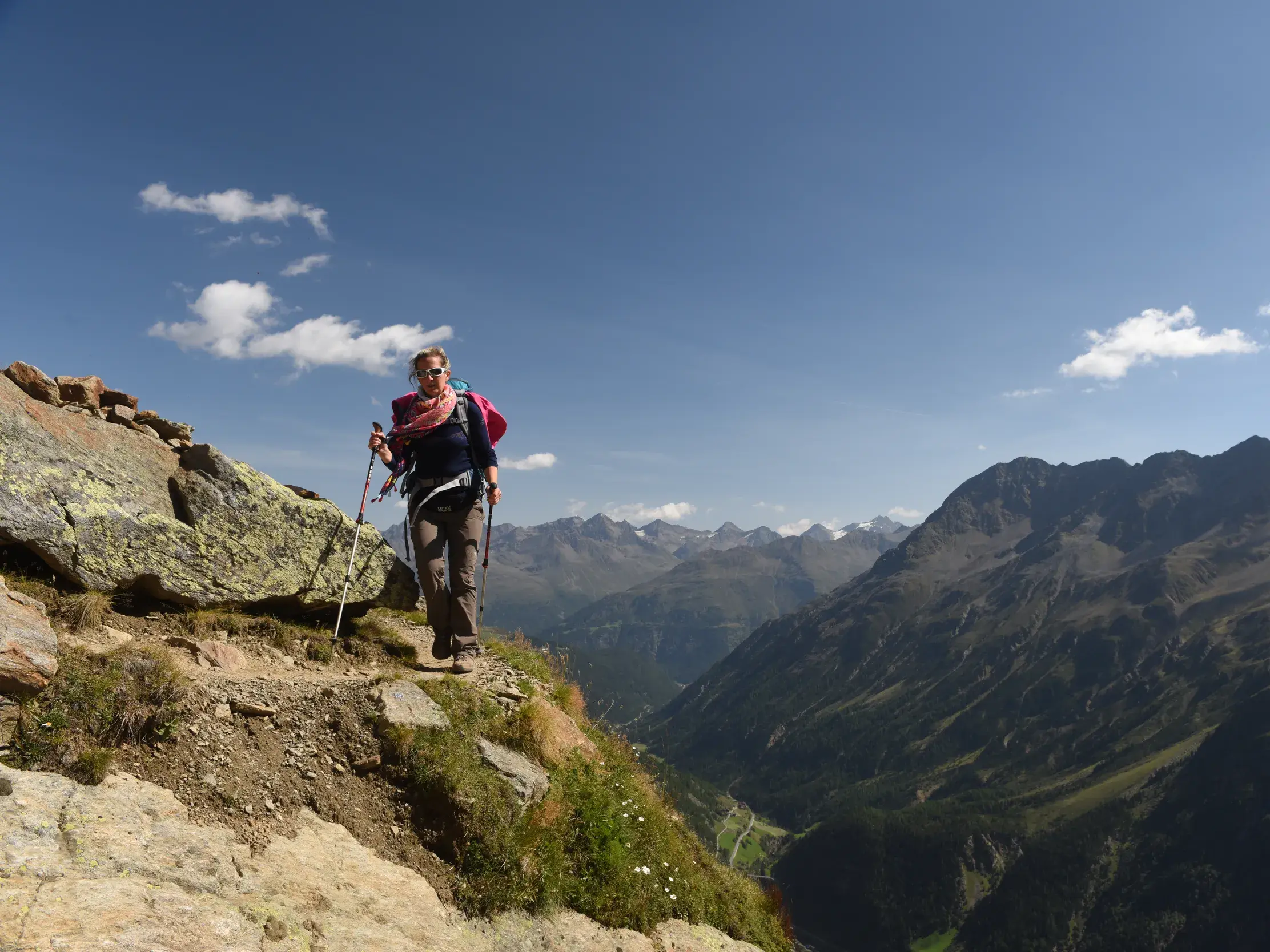 Wanderin auf einem schmalen Bergpfad während der Alpenüberquerung E5 mit weitem Panoramablick auf die Täler der Alpen.
