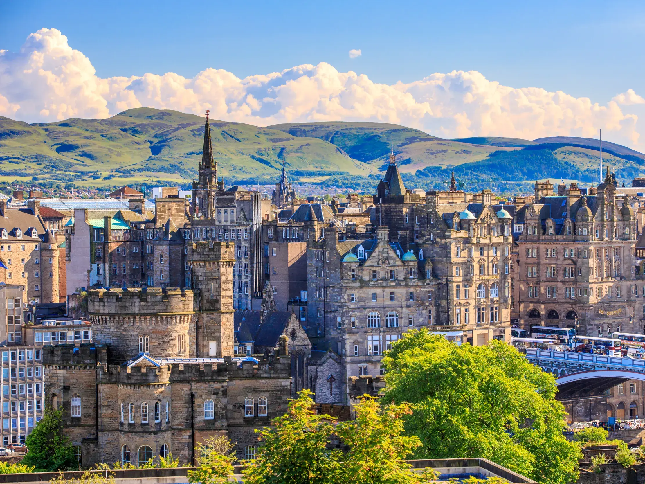 Sonniger Panoramablick über die historische Altstadt von Edinburgh mit ihren Türmen und gotischen Gebäuden vor der Hügelkette des Arthur's Seat.