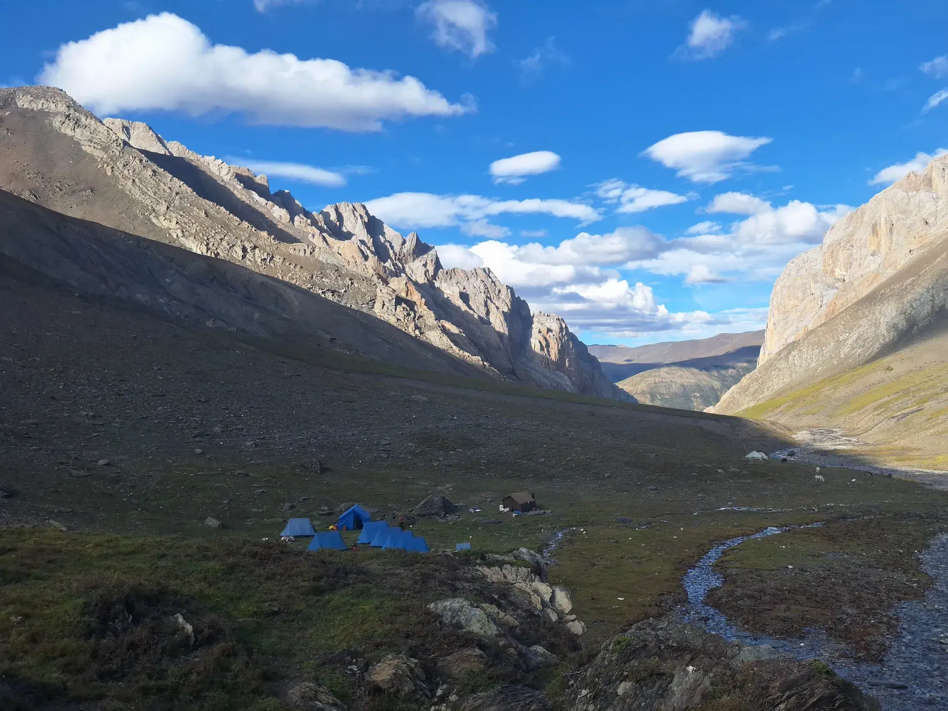 Blaues Zeltlager einer Trekking-Reise in einem abgeschiedenen, weiten Tal in der Dolpo-Region, Nepal, umgeben von hohen Bergen.