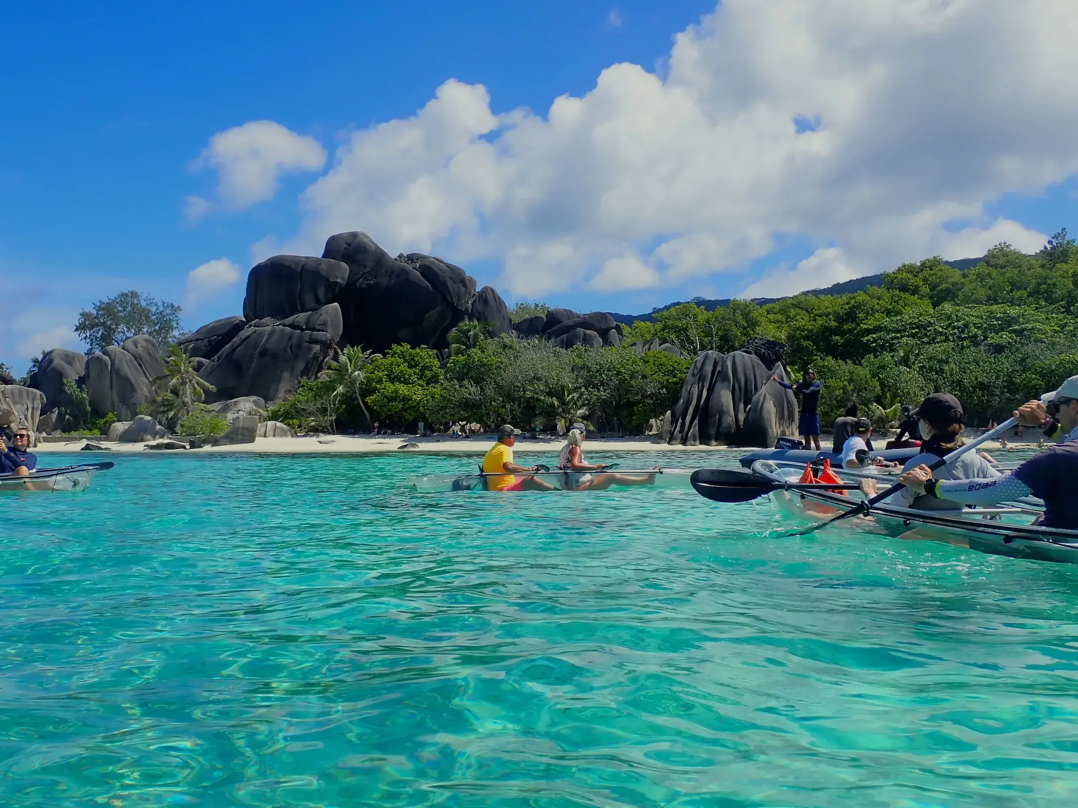 Reisegruppe auf Kajaktour im türkisblauen Meer vor den Granitfelsen des Strandes Source d'Argent auf La Digue.