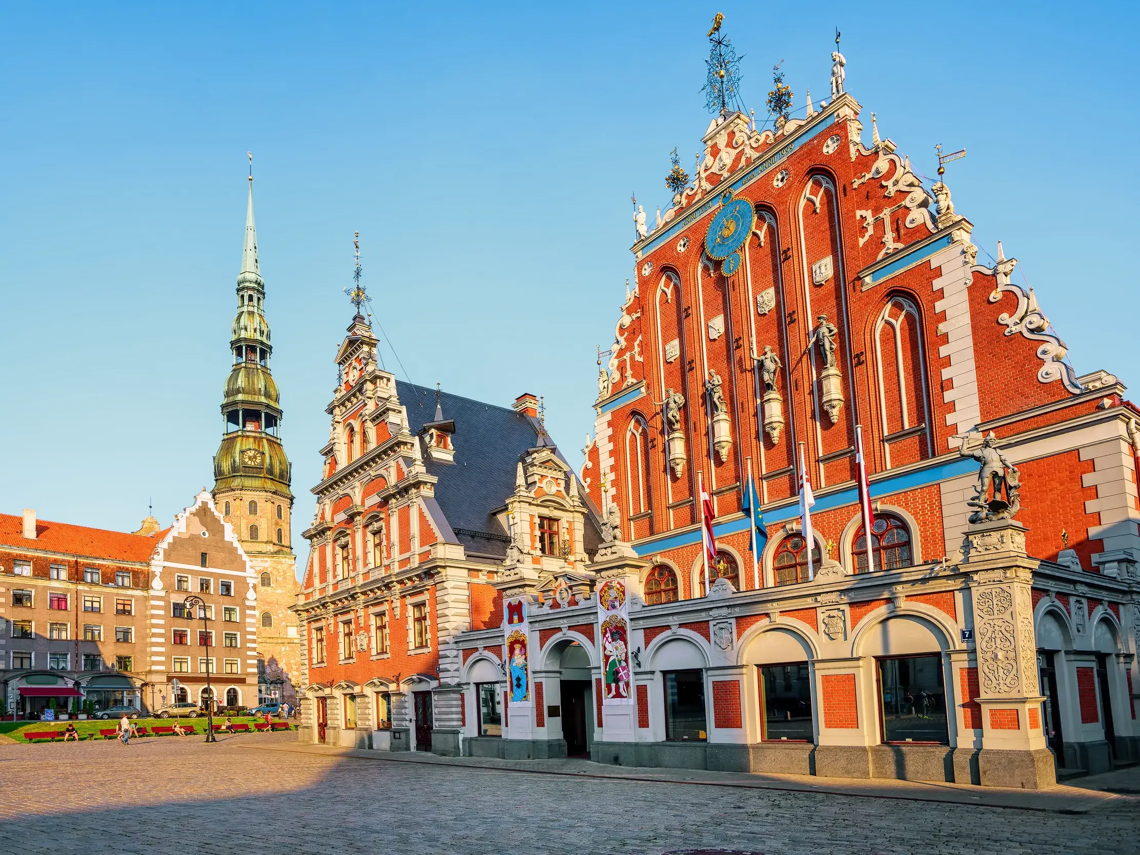 Das prachtvolle Schwarzhäupterhaus in Riga und die Petrikirche auf dem Rathausplatz, beleuchtet von der goldenen Abendsonne.