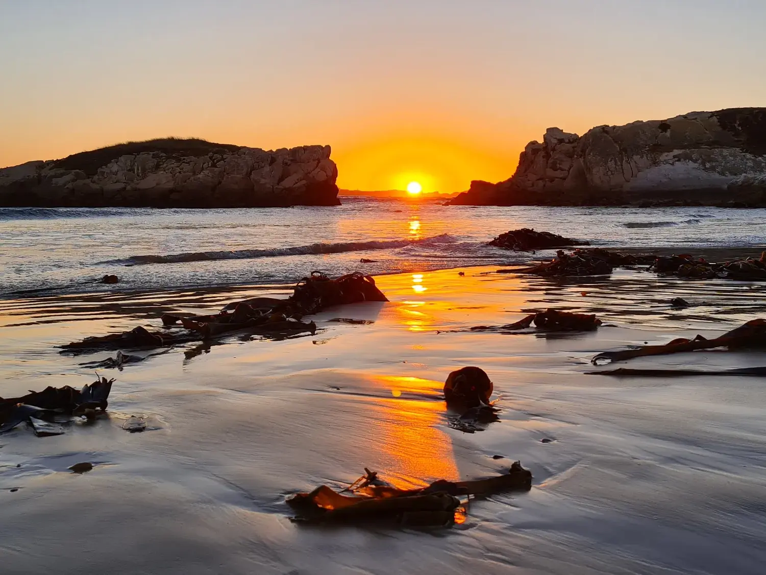 Abenddämmerung am Strand von Peniche: Die Sonne geht zwischen zwei Felsklippen unter und wirft goldene Reflexionen auf den Sand.