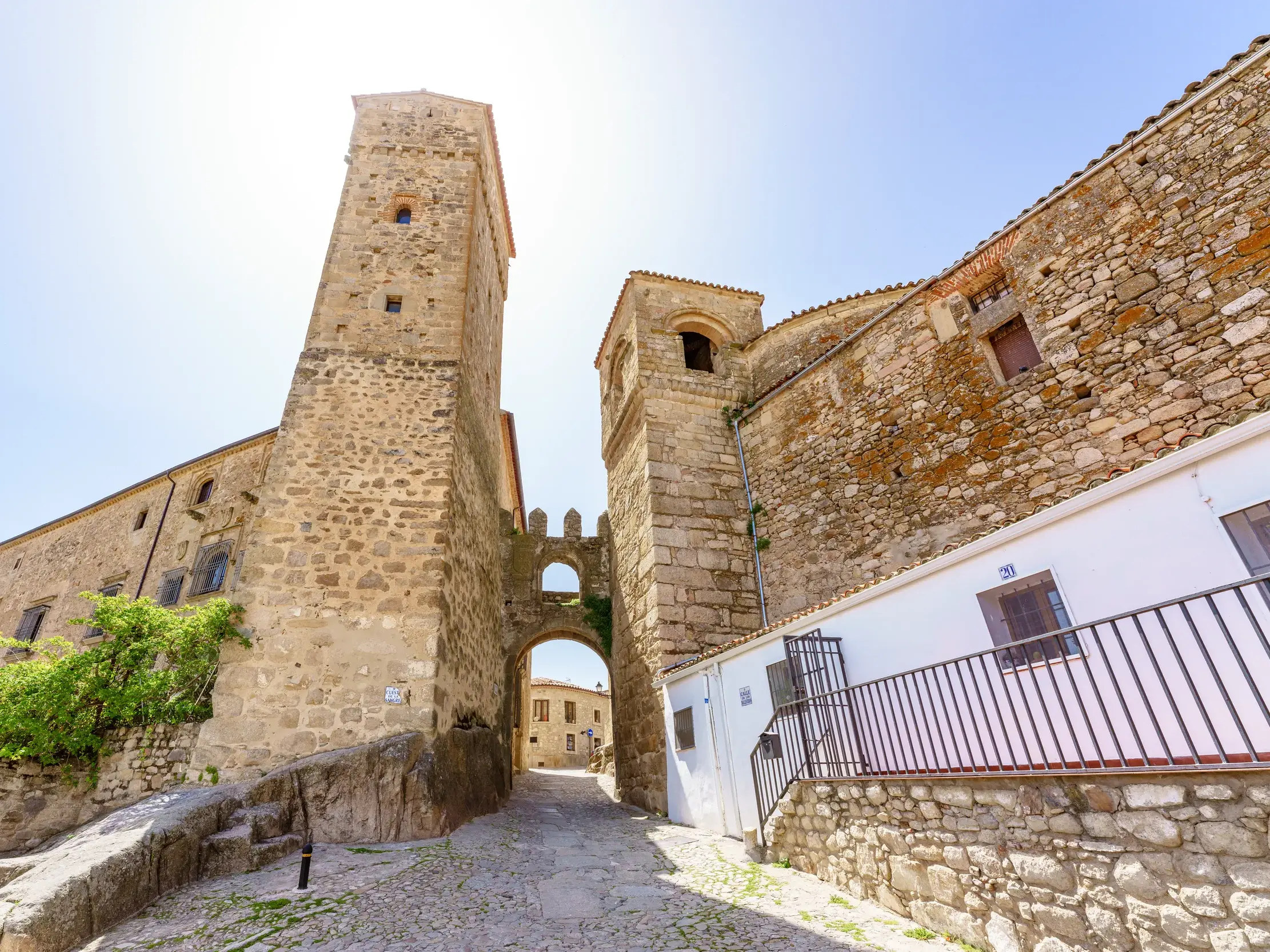 Eine gepflasterte Gasse führt durch ein historisches Stadttor mit Türmen in die Altstadt von Trujillo.