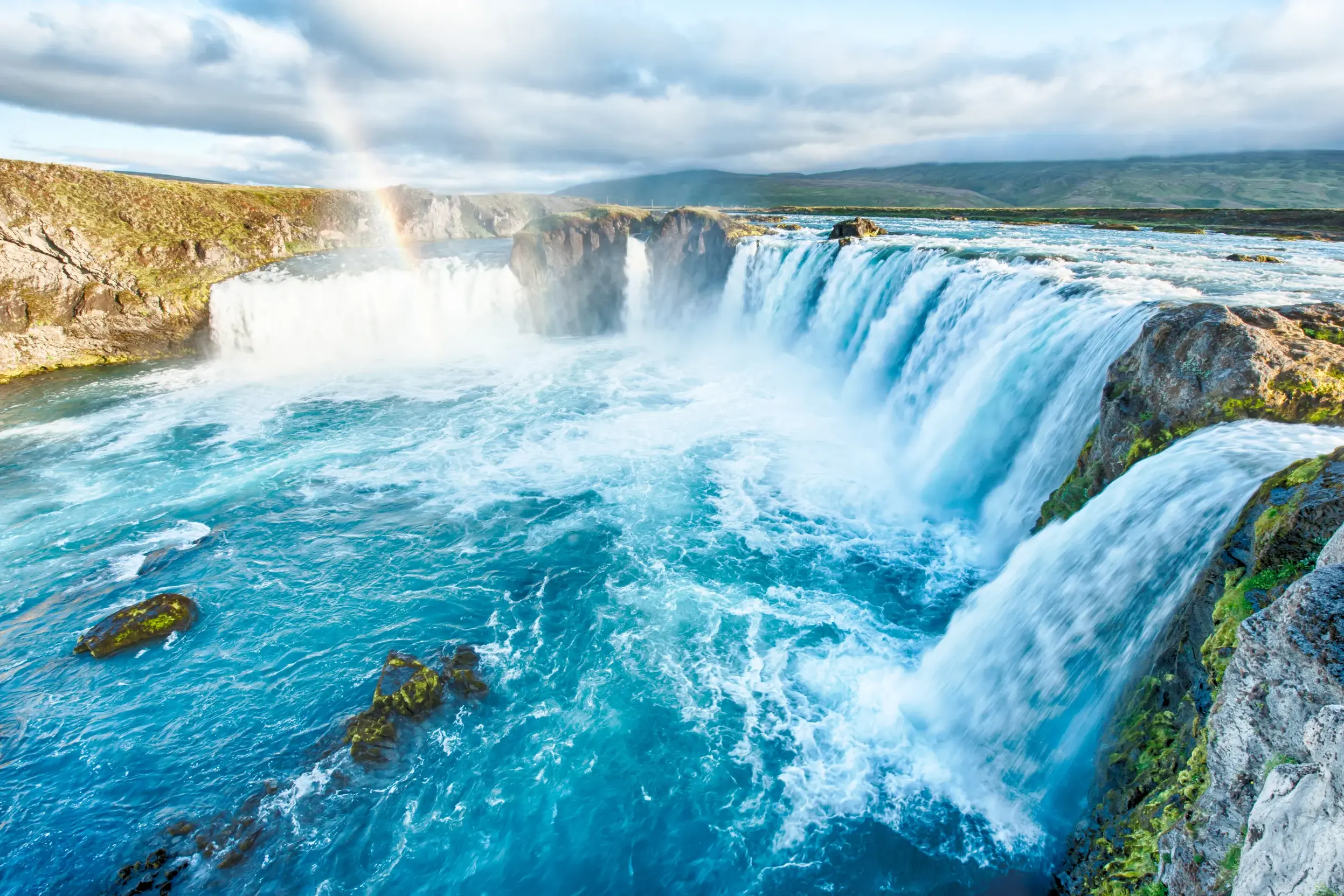 Tosende Wassermassen des Godafoss in Island stürzen über breite Felsklippen in ein leuchtend türkises Flussbett.