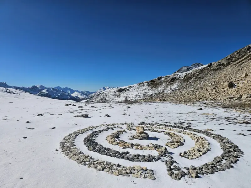 Eine von Hand gelegte Steinspirale in einer verschneiten Hochebene bei einer Wanderung in den Graubündner Alpen.