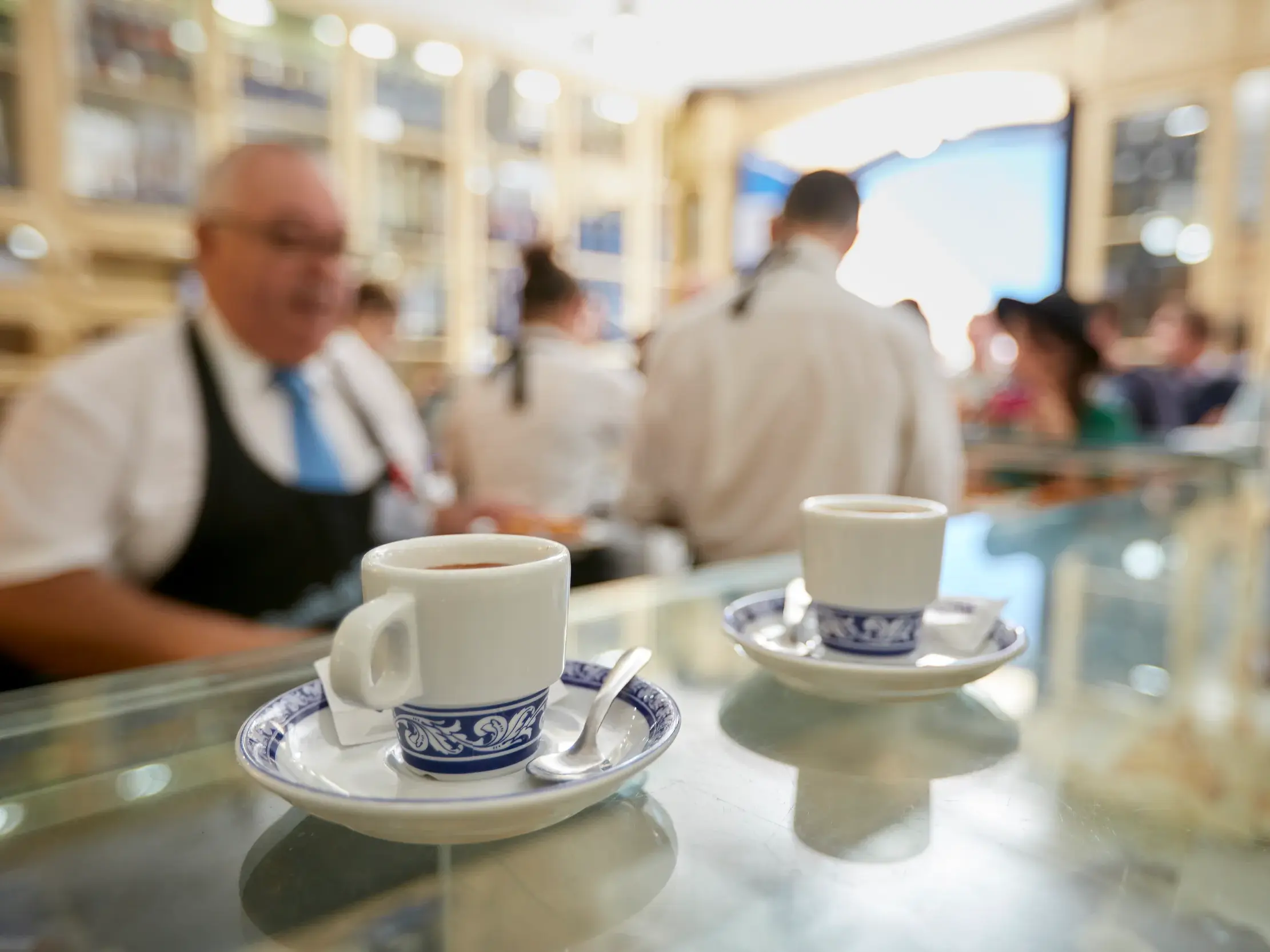 Zwei traditionelle Kaffeetassen mit blauen Mustern auf der Theke eines belebten Cafés während einer Portugal-Reise.