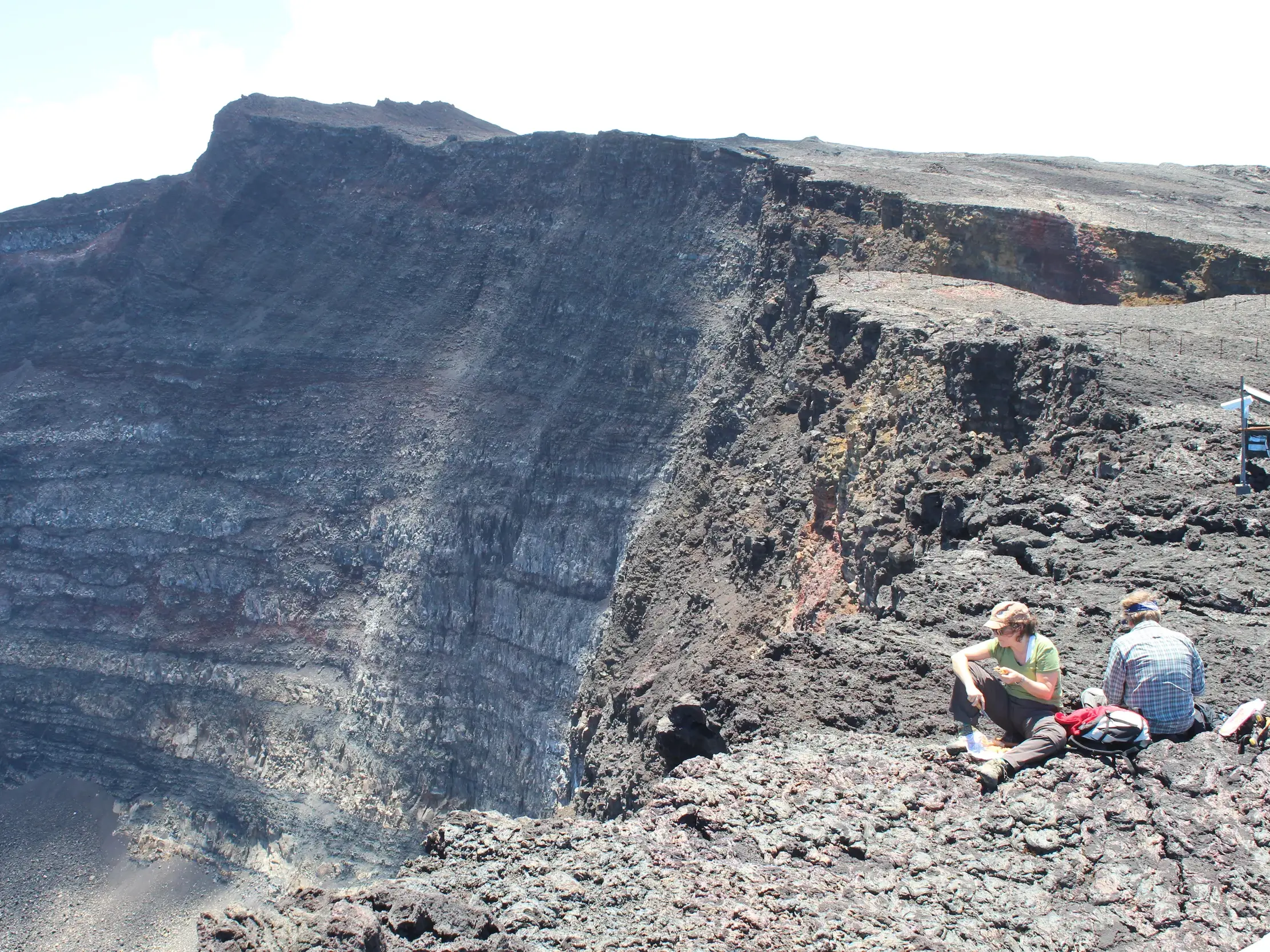Zwei Wanderer bei einer Trekking-Pause am steilen Kraterrand des Vulkans Piton de la Fournaise auf La Réunion.