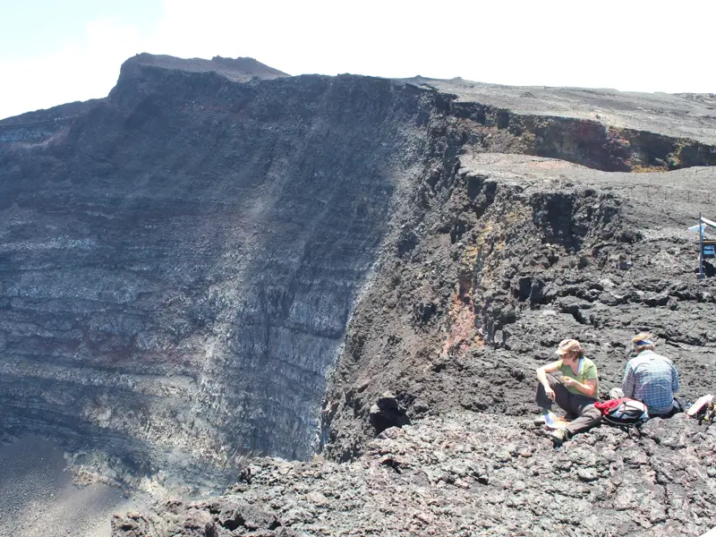 Zwei Wanderer bei einer Trekking-Pause am steilen Kraterrand des Vulkans Piton de la Fournaise auf La Réunion.