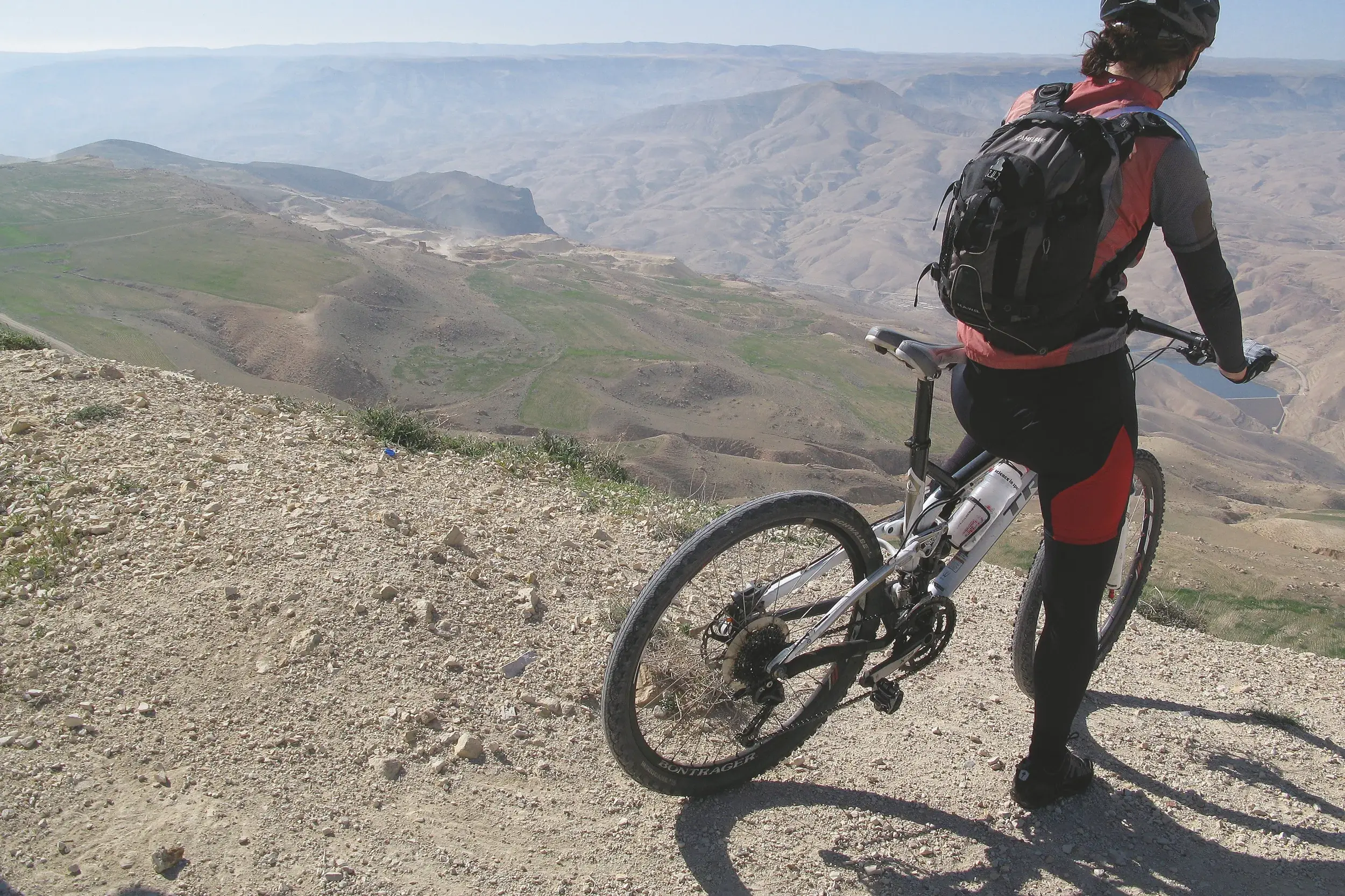 Eine Mountainbikerin pausiert auf einer Anhöhe und genießt den weiten Panoramablick über Jordaniens sonnige Wüstenlandschaft.
