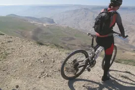 Eine Mountainbikerin pausiert auf einer Anhöhe und genießt den weiten Panoramablick über Jordaniens sonnige Wüstenlandschaft.