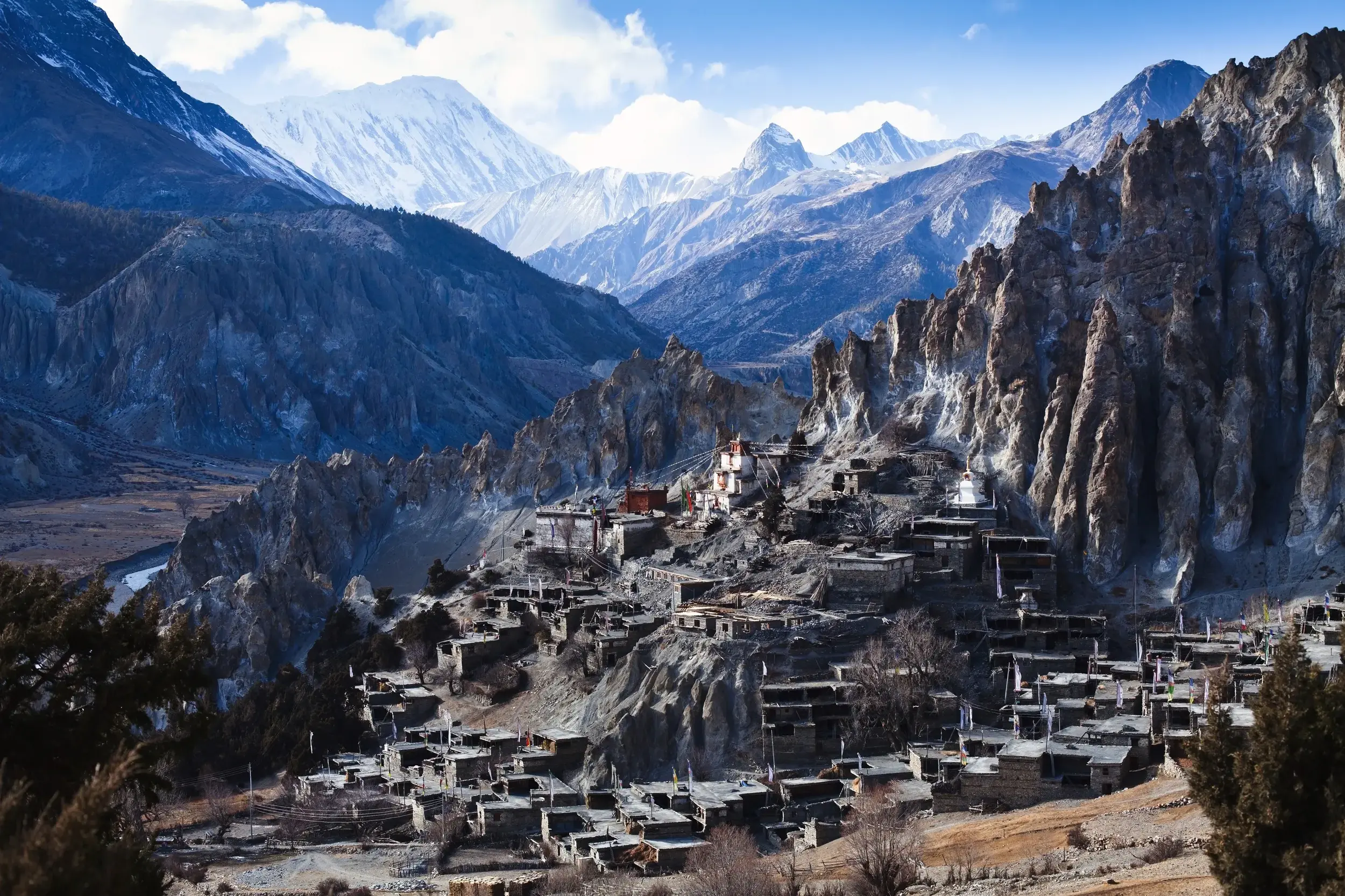 Das Bergdorf Manang mit Flachdachhäusern, erbaut an einem Felsenhang vor dem schneebedeckten Annapurna-Massiv in Nepal.