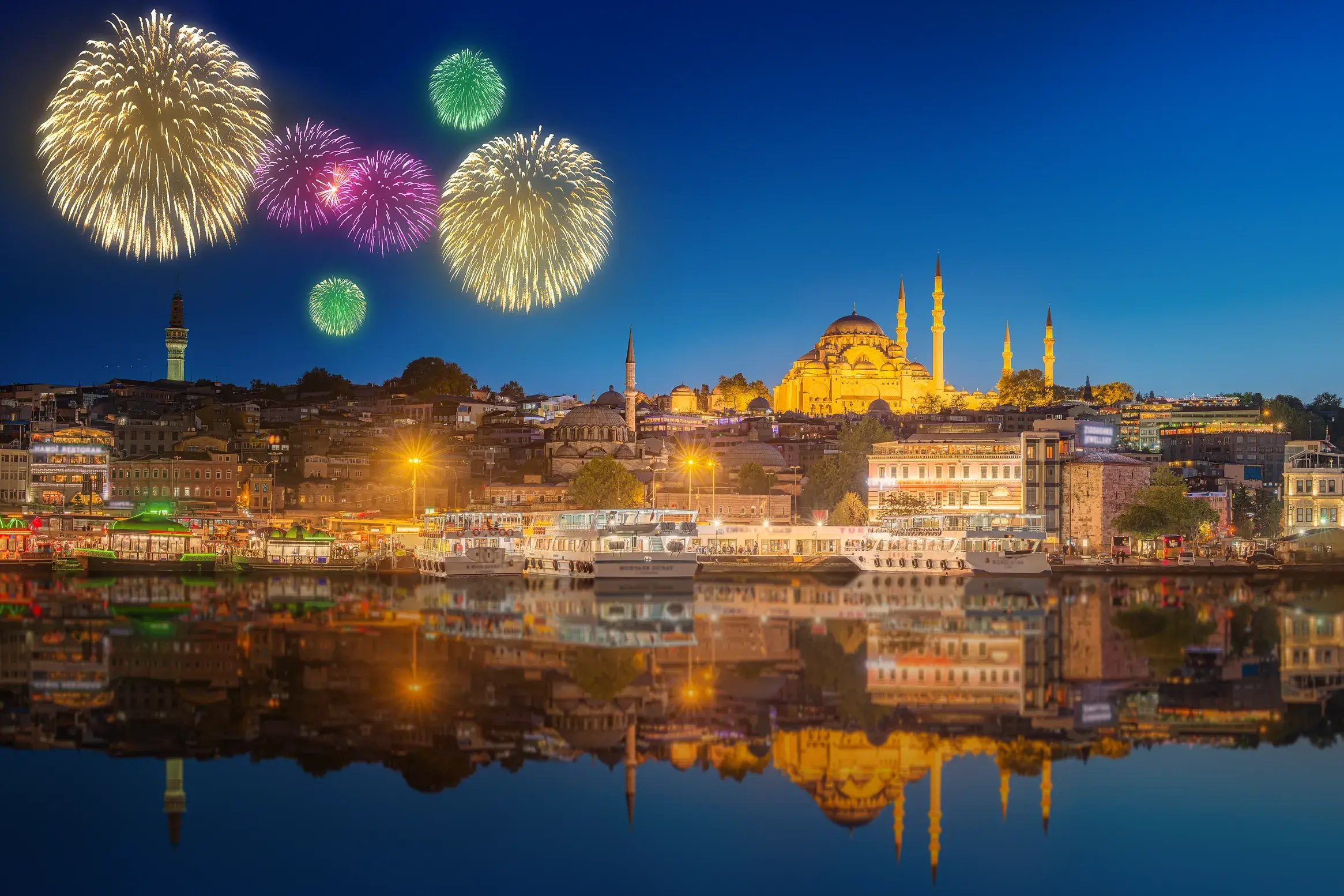Buntes Silvester-Feuerwerk über Istanbul mit Blick auf die beleuchtete Süleyman-Moschee, die sich im Goldenen Horn spiegelt.