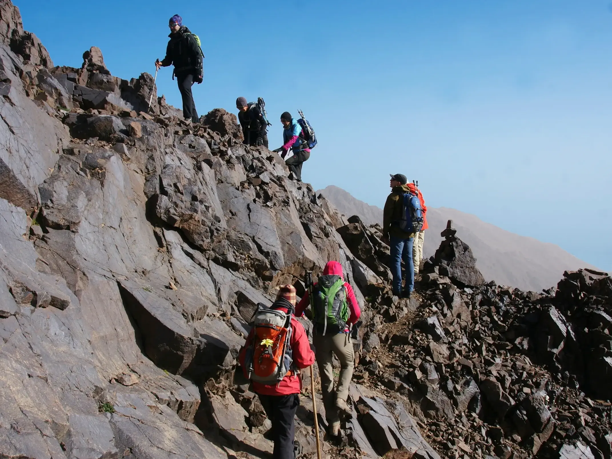 Eine Hauser-Reisegruppe beim anspruchsvollen Trekking auf einem steilen, felsigen Grat auf dem Weg zum Gipfel im Hohen Atlas.
