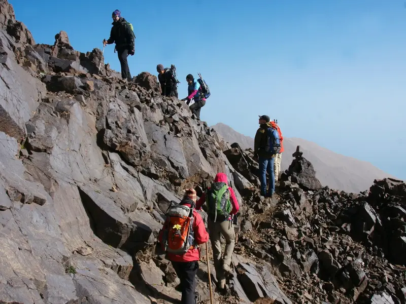 Eine Hauser-Reisegruppe beim anspruchsvollen Trekking auf einem steilen, felsigen Grat auf dem Weg zum Gipfel im Hohen Atlas.