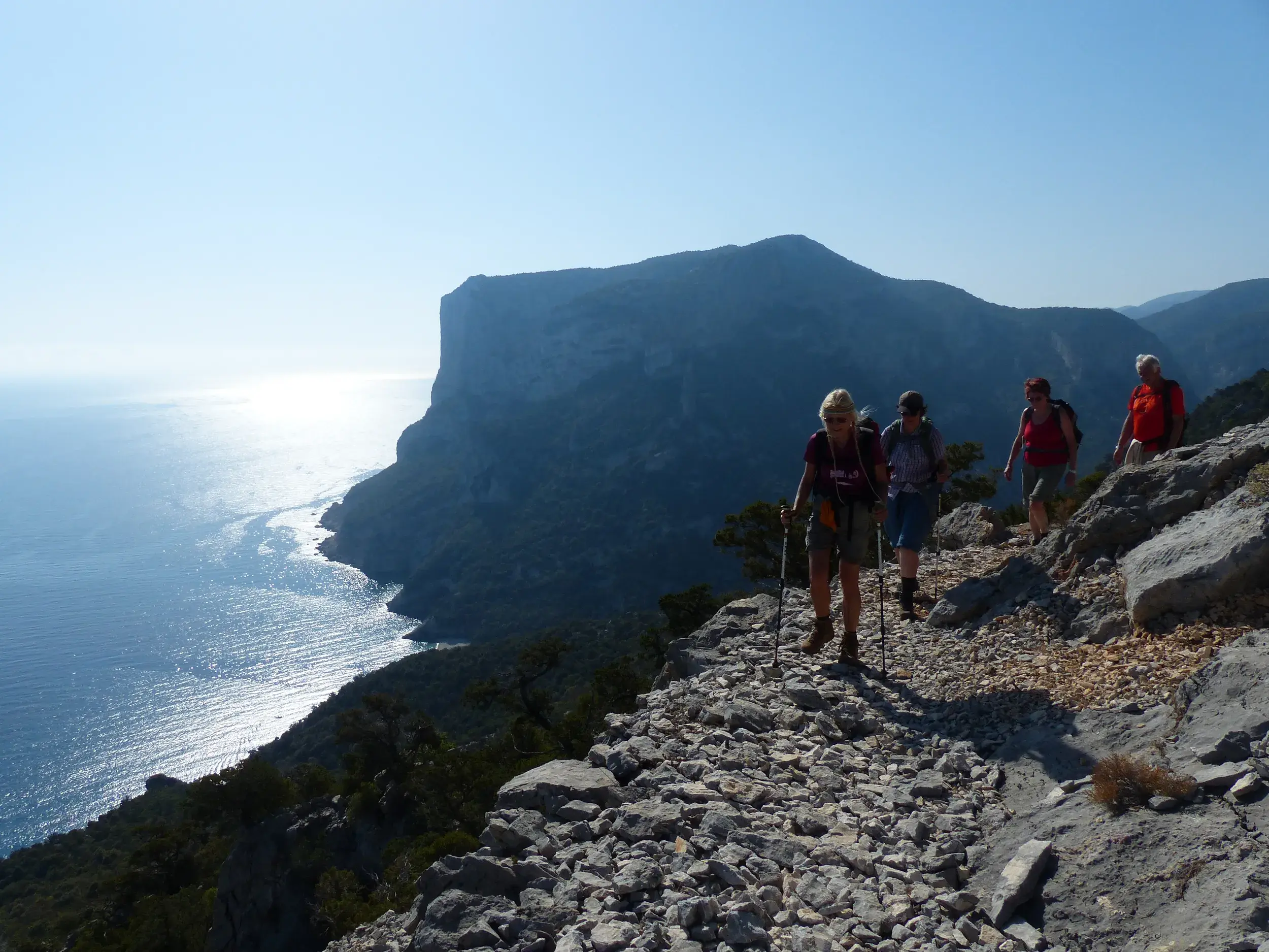 Kleine Wandergruppe auf einem felsigen Küstenpfad mit Panoramablick auf die Steilküste und das Meer am Golf von Orosei.