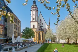 Historische Thomaskirche in Leipzig mit Kirchturm hinter einer grünen Parkanlage mit Frühlingsblüten