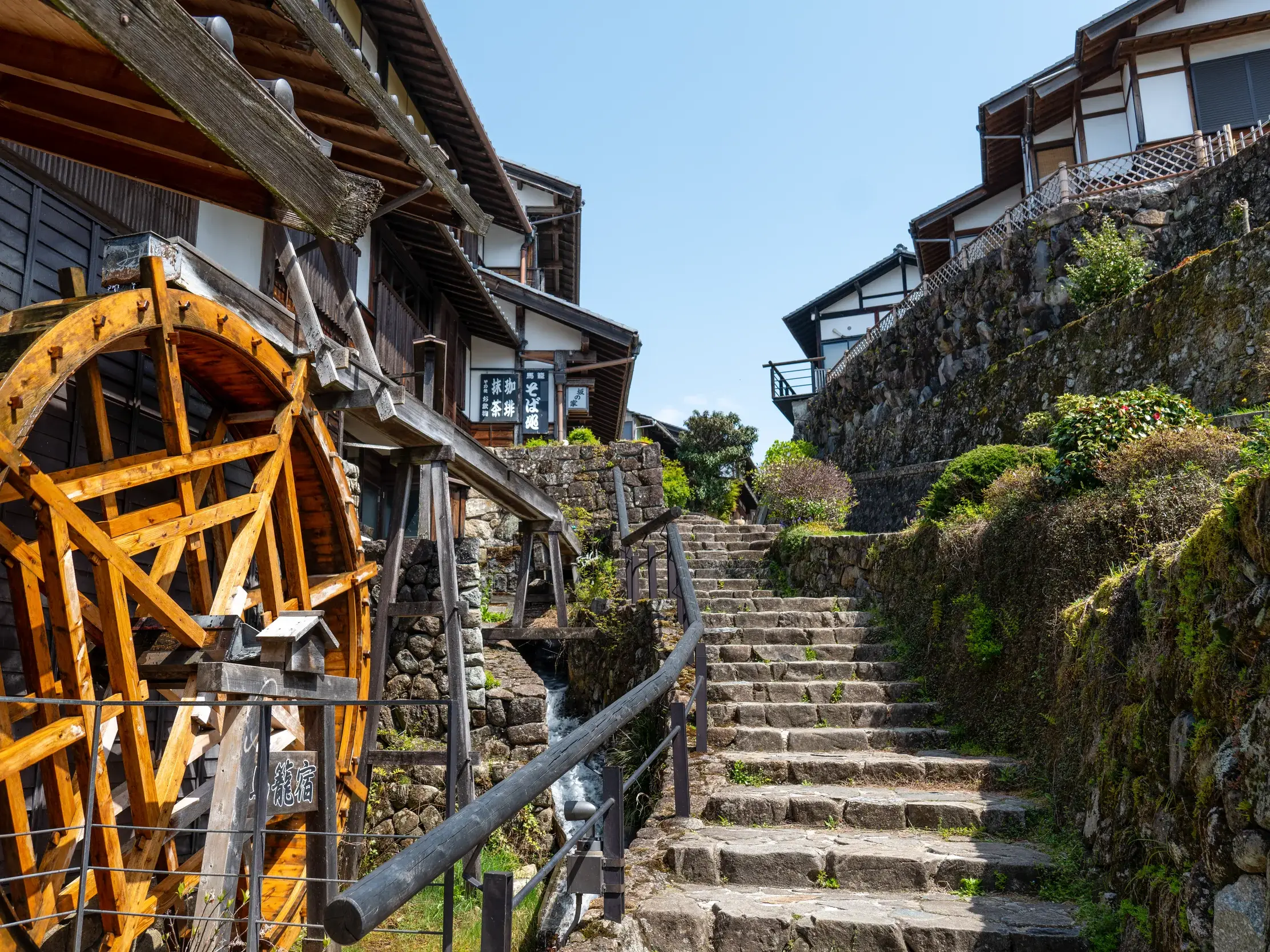 Altes Holzwasserrad neben einer Steintreppe im historischen Poststationsort Magome an der Nakasendo-Route im Kiso-Tal.