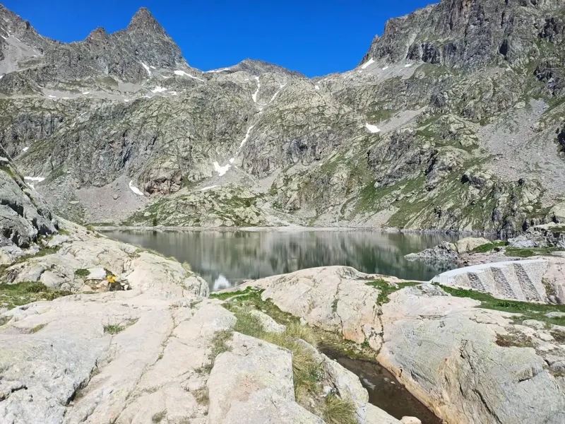 Ruhiger Bergsee mit kleiner Staumauer, umgeben von felsigen Gipfeln in den französischen Seealpen nahe Nizza.