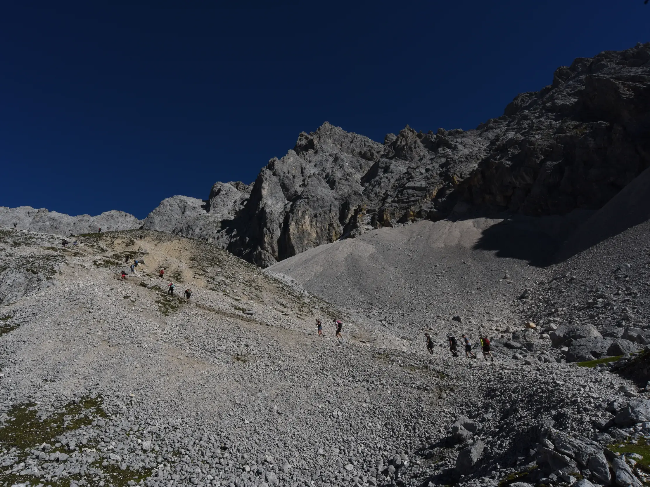 Eine Hauser-Reisegruppe steigt über die kargen, geröllreichen Moränen am Zugspitzplatt in Richtung Gipfel der Zugspitze auf.