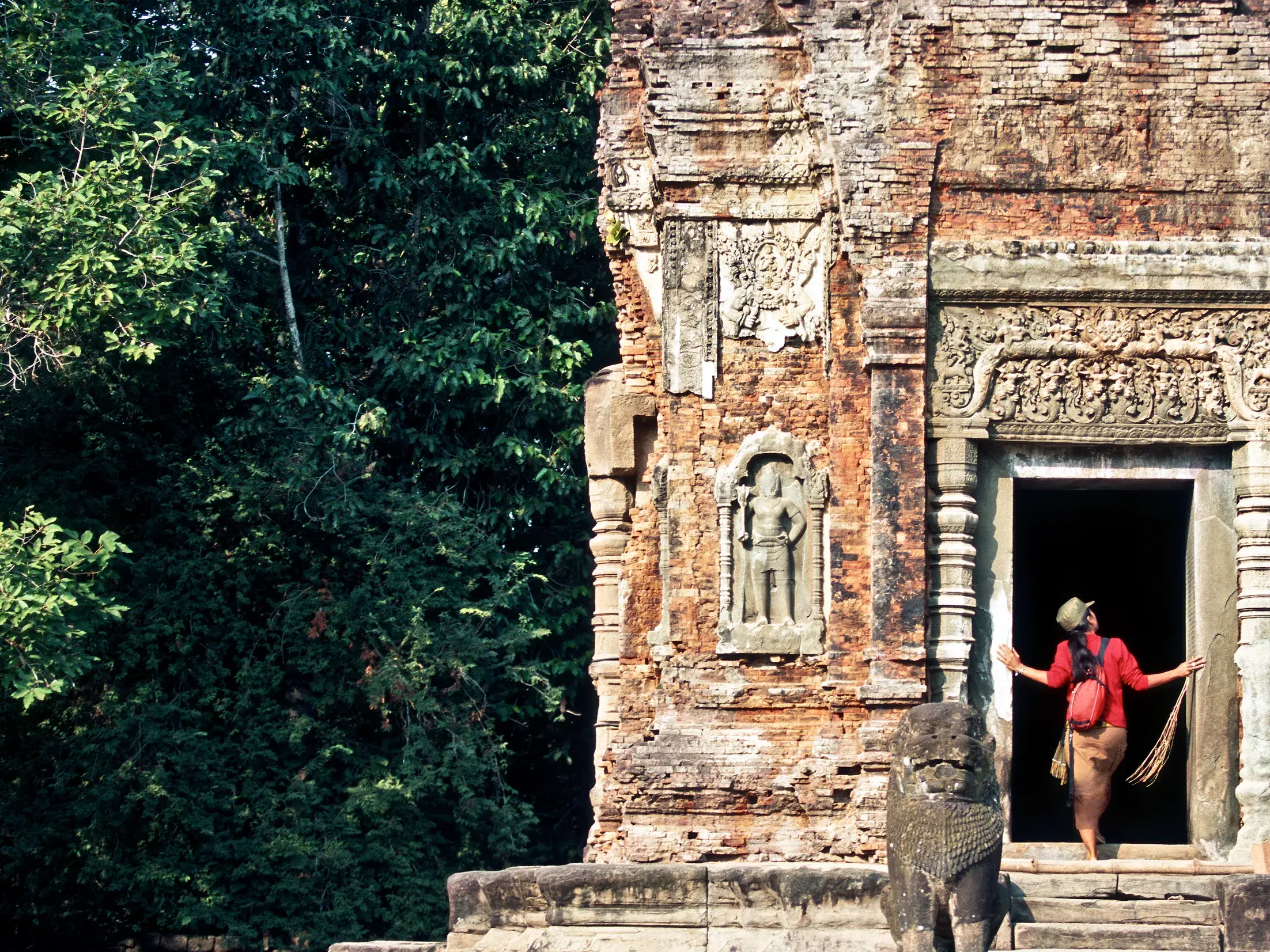 Eine Frau erkundet auf ihrer geführten Rundreise den Eingang eines von Dschungel umgebenen Tempels in Angkor.