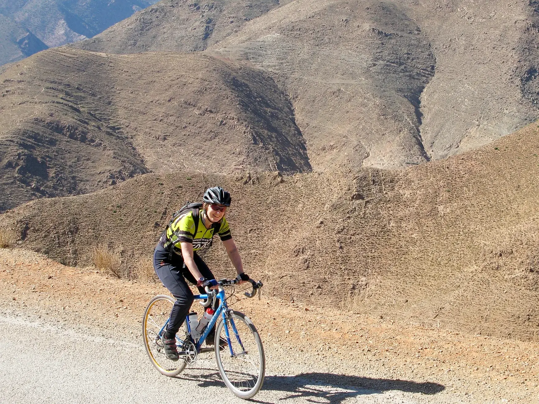 Lächelnde Rennradfahrerin auf einer geführten Rundreise durch die sonnige und karge Berglandschaft des Hohen Atlas in Marokko.