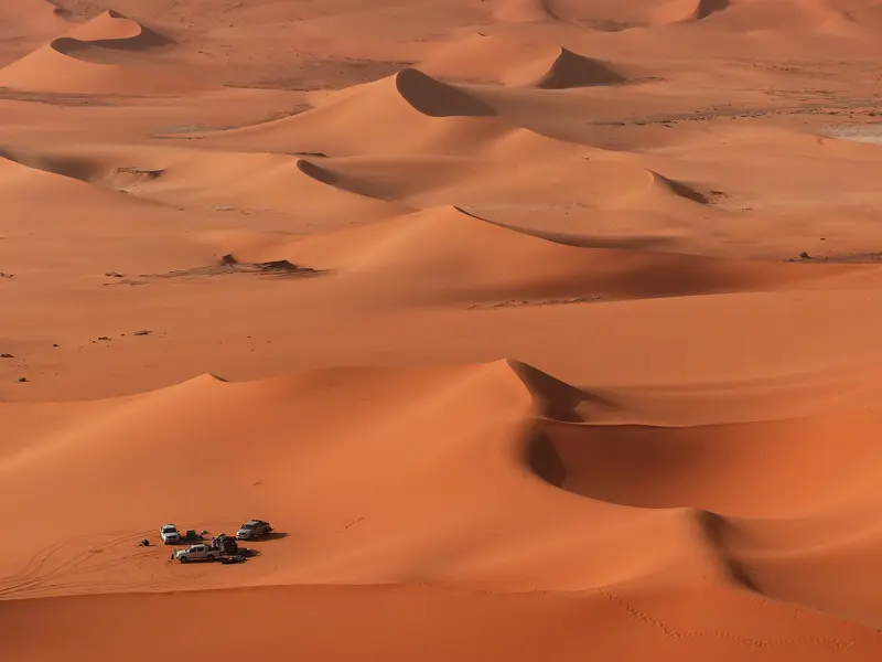 Drei Geländewagen einer Trekking-Expedition rasten in der unendlichen Weite der orangefarbenen Sanddünen des Erg Admer.