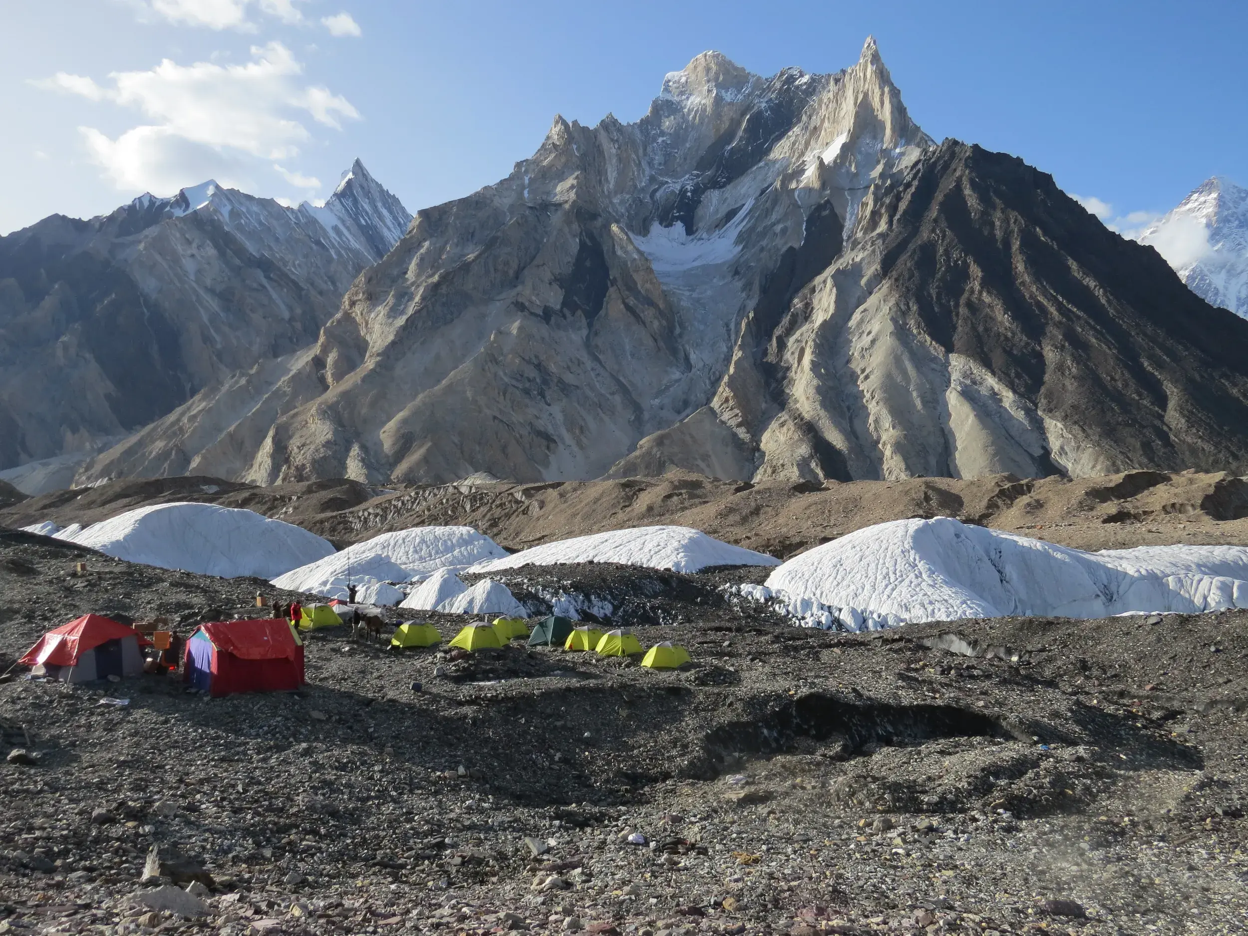 Farbenfrohes Zeltlager einer Trekkinggruppe auf der Gesteinsmoräne am Concordia-Platz, umgeben von Gletschern und den Eisriesen des Karakorum.