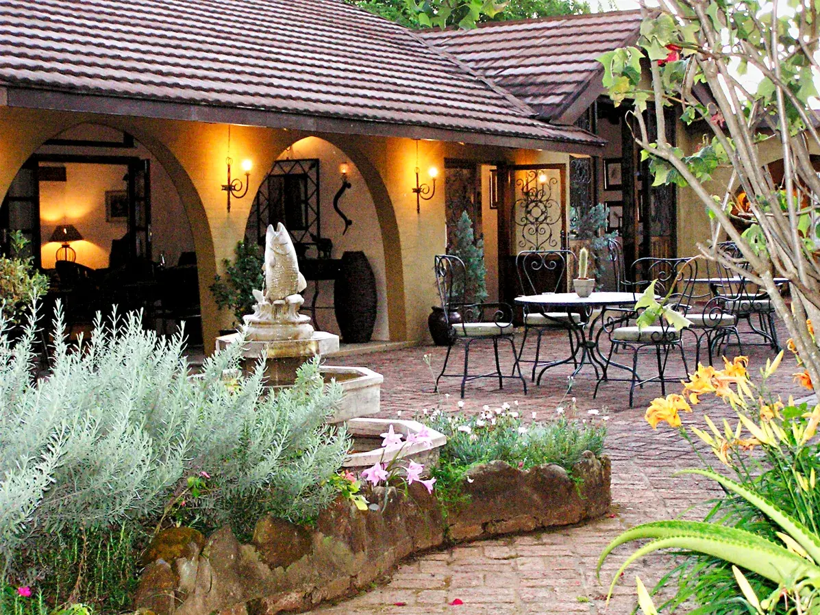 Idyllische Terrasse des Böhm's Zeederberg Country House bei Sabie mit einem Brunnen, üppigen Pflanzen und Sitzplätzen am Abend.