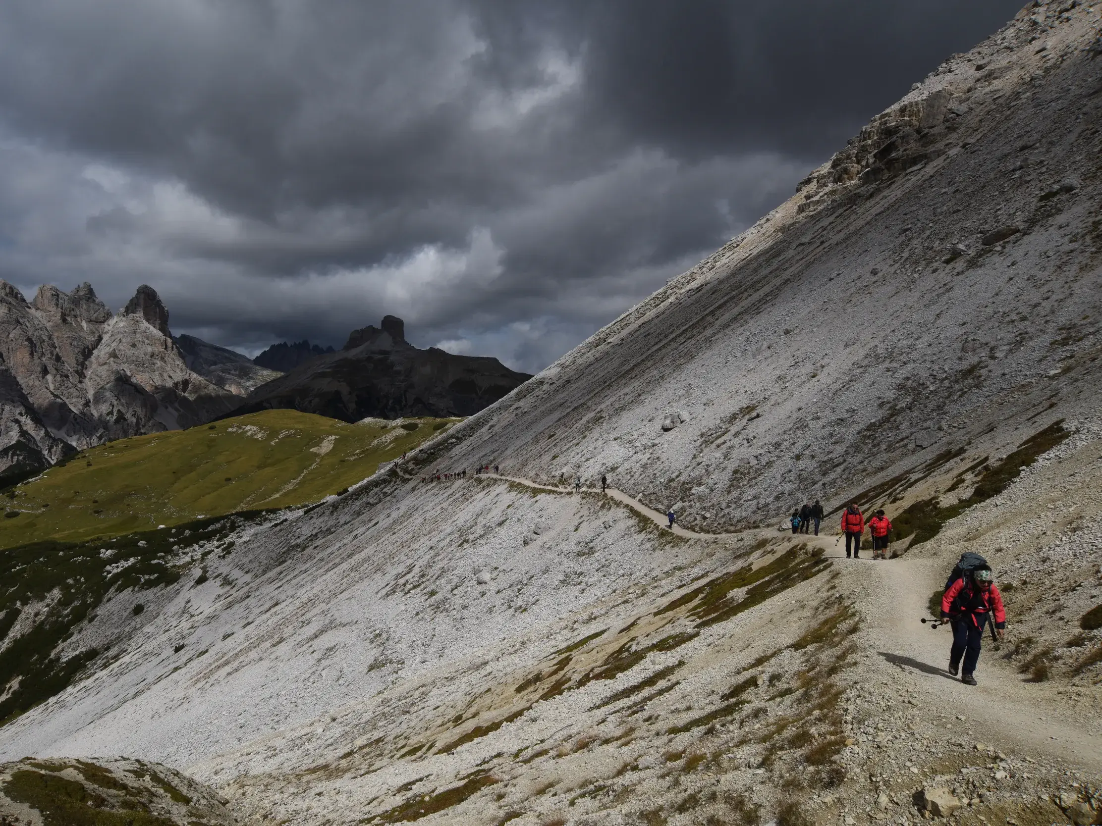 Eine Trekkinggruppe wandert auf einem schmalen Geröllpfad entlang eines steilen Berghangs im UNESCO Welterbe Dolomiten.