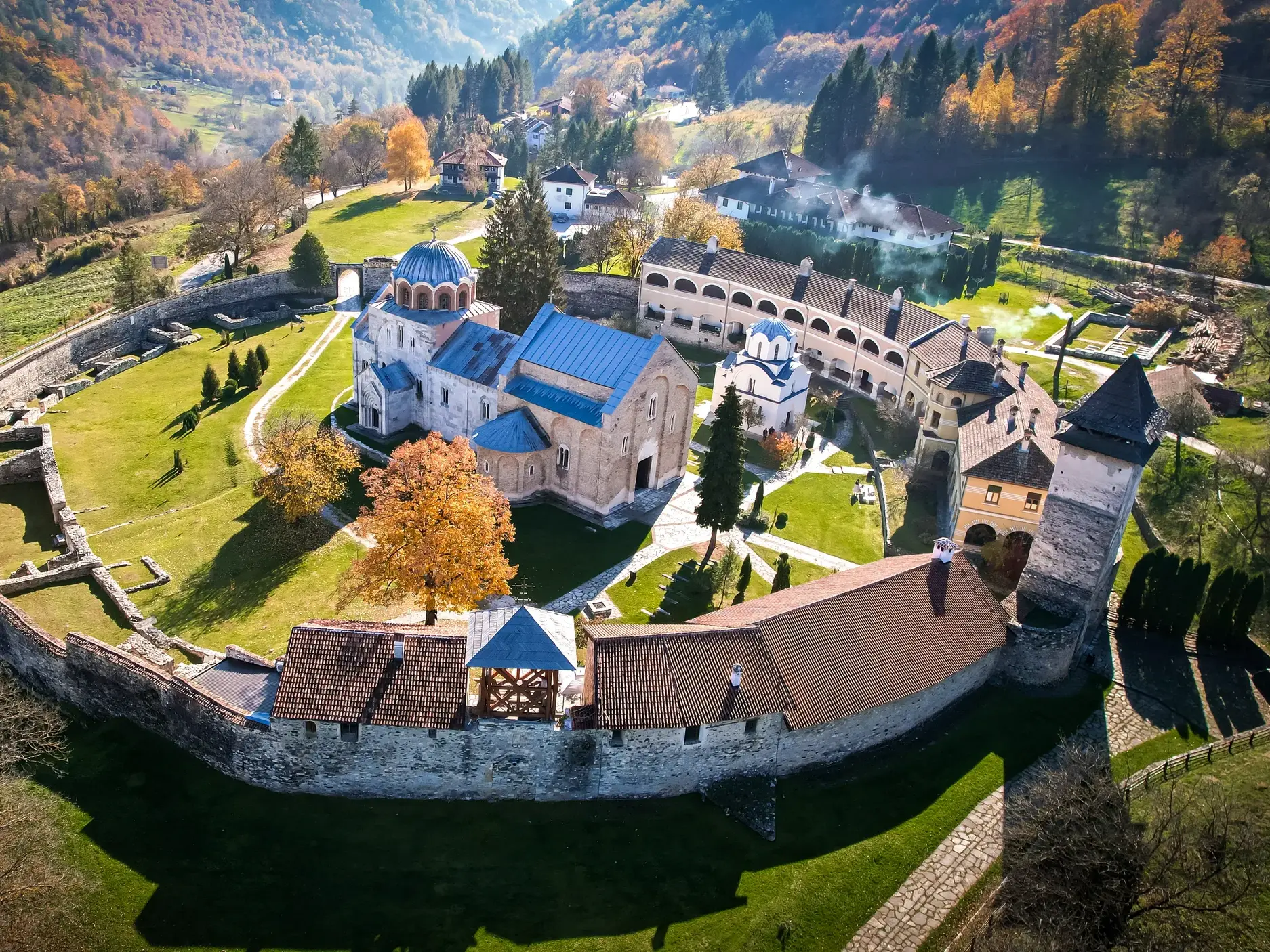 Luftaufnahme des Klosters Studenica, UNESCO-Welterbe in Serbien, umgeben von einer Wehrmauer in einer herbstlichen Tallandschaft.