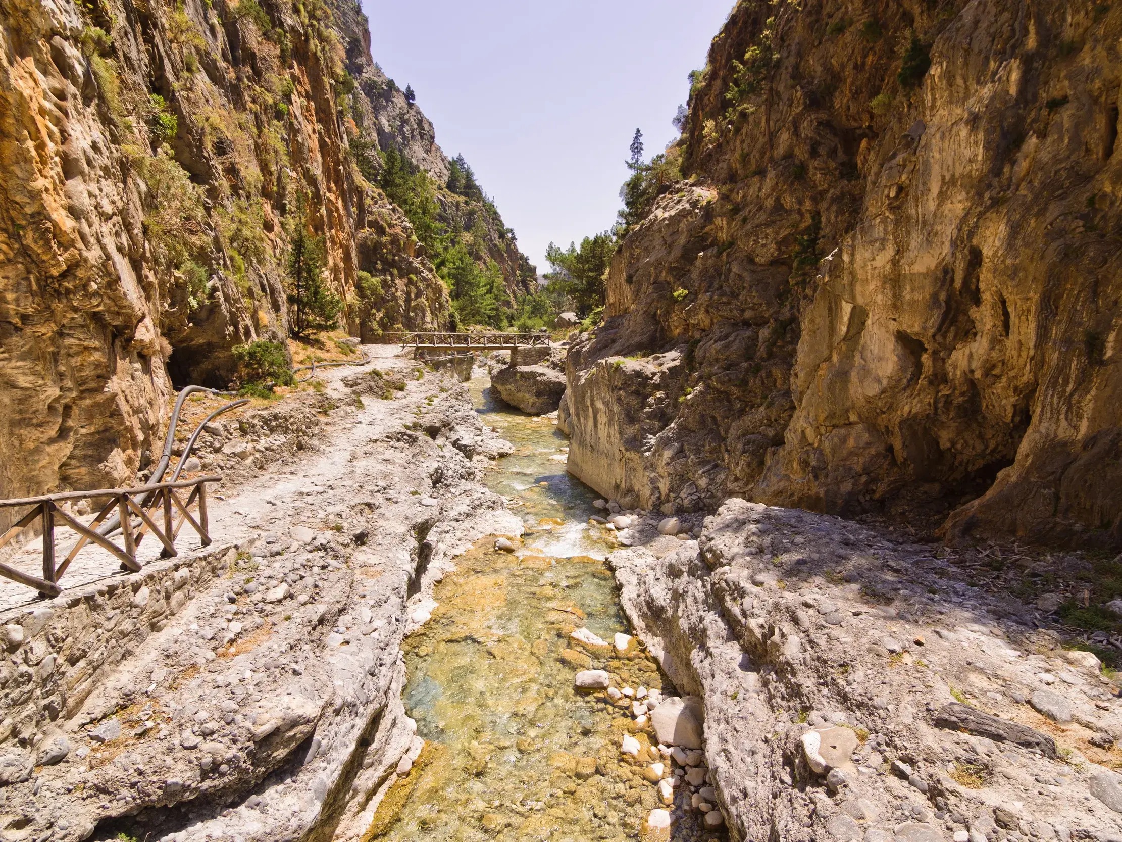 Ein steiniger Wanderpfad schlängelt sich entlang eines Baches durch die imposante, sonnige Samaria-Schlucht auf Kreta.