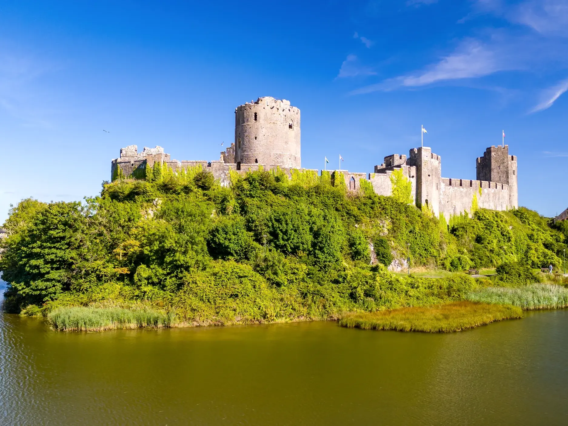 Das imposante Pembroke Castle in Wales, umgeben von einem Wassergraben und üppigem Grün an einem sonnigen Sommertag.